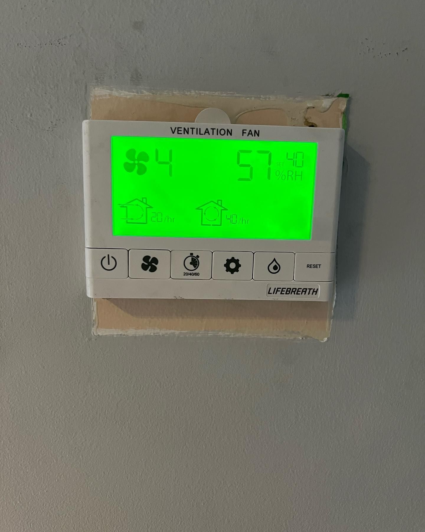 A white thermostat with a green screen that says ventilation fan