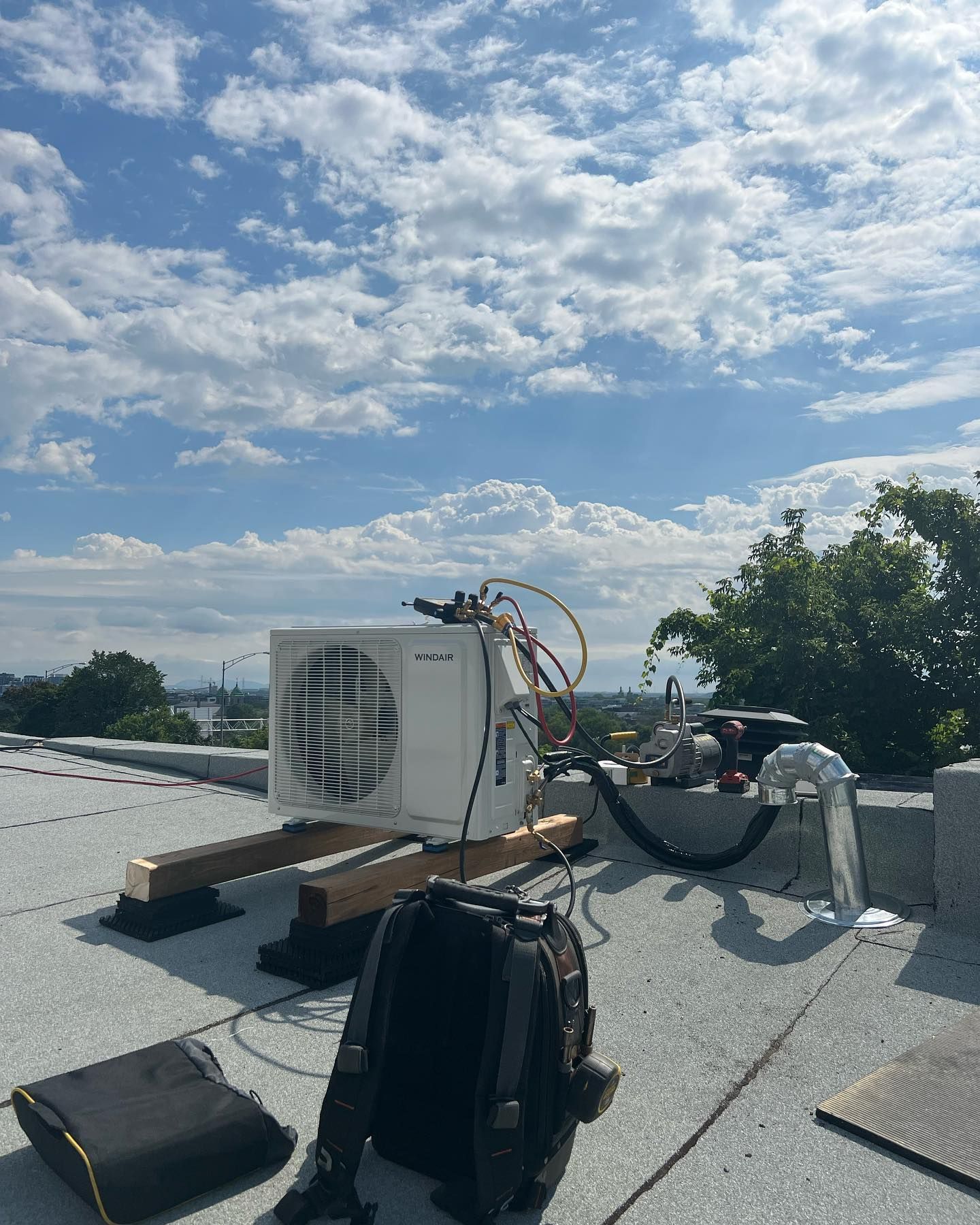 An air conditioner is sitting on top of a roof next to a backpack.