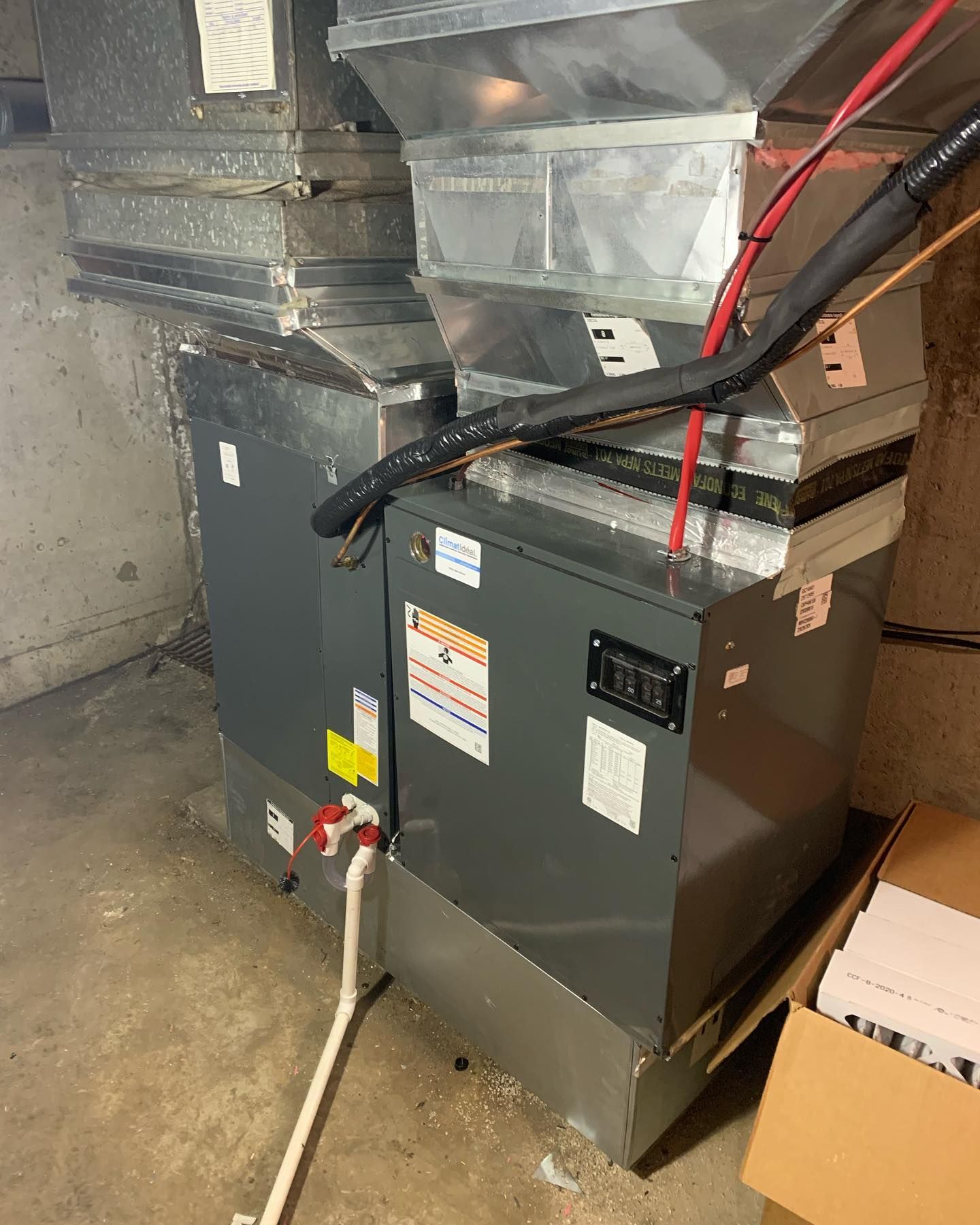 An air conditioner is sitting in a basement next to a box.