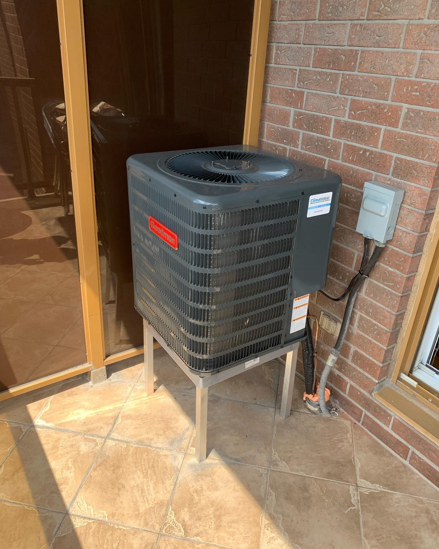 An air conditioner is sitting on top of a metal stand on a patio next to a brick wall.