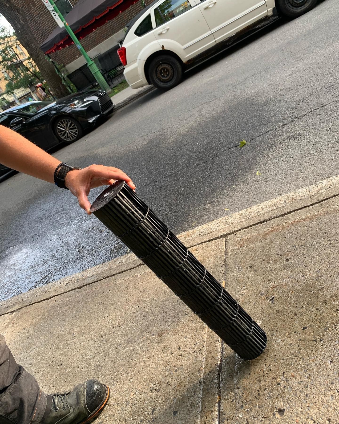 A person is holding a fan on the sidewalk in front of a car.