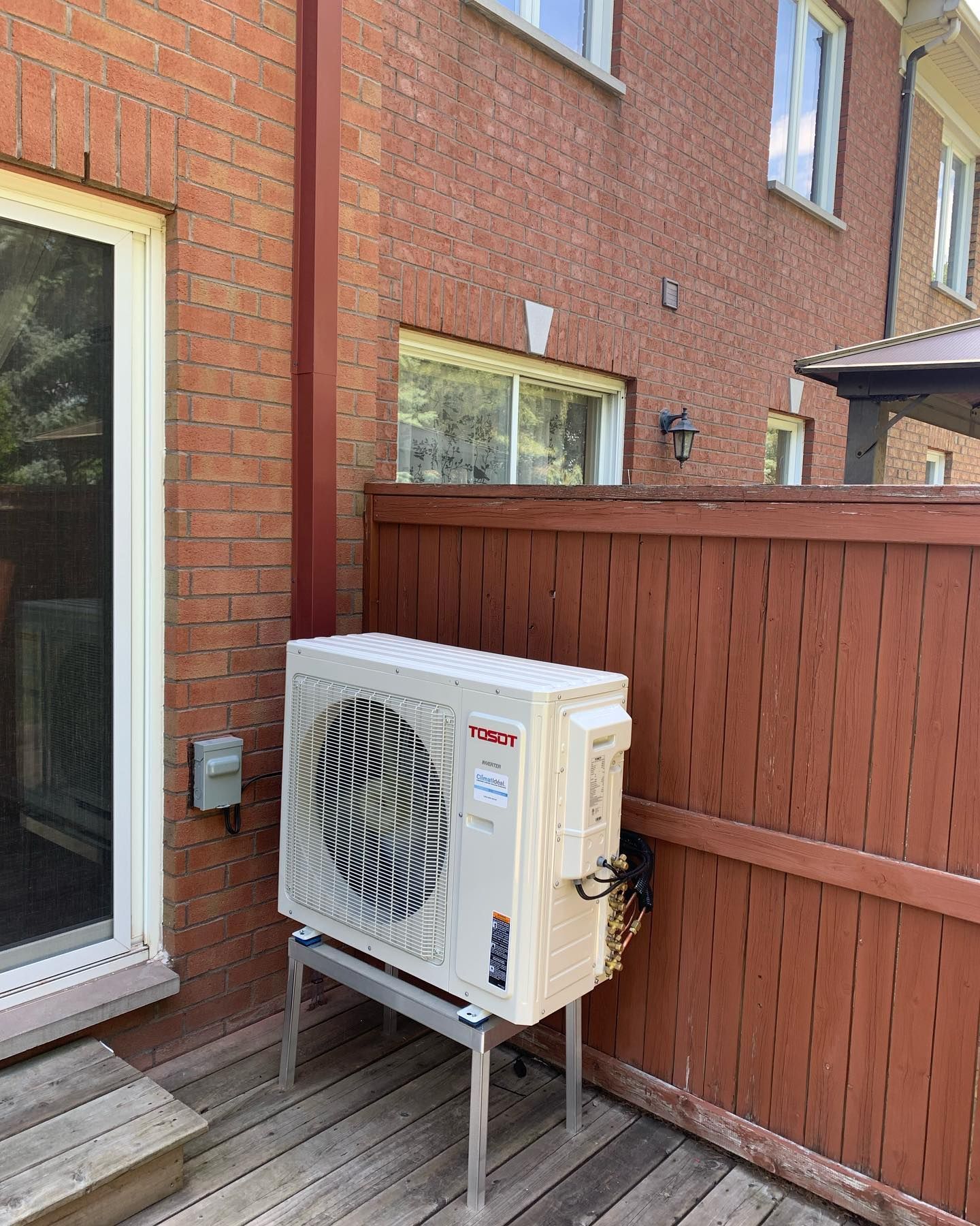 A white air conditioner is sitting on a wooden deck next to a brick building.