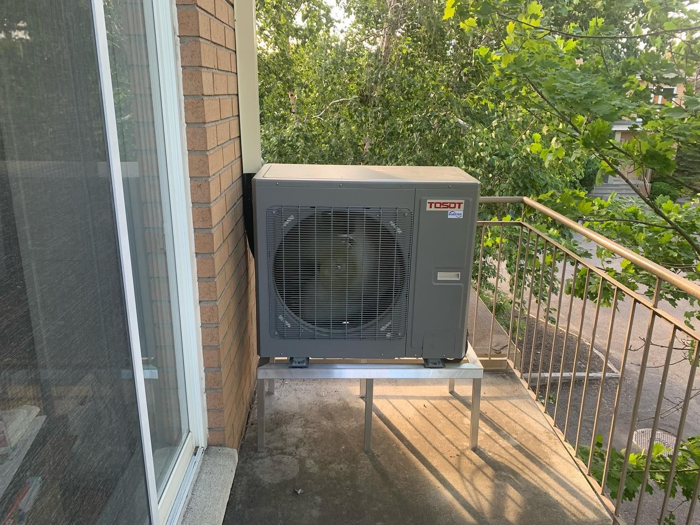 A large air conditioner is sitting on a balcony next to a brick building.