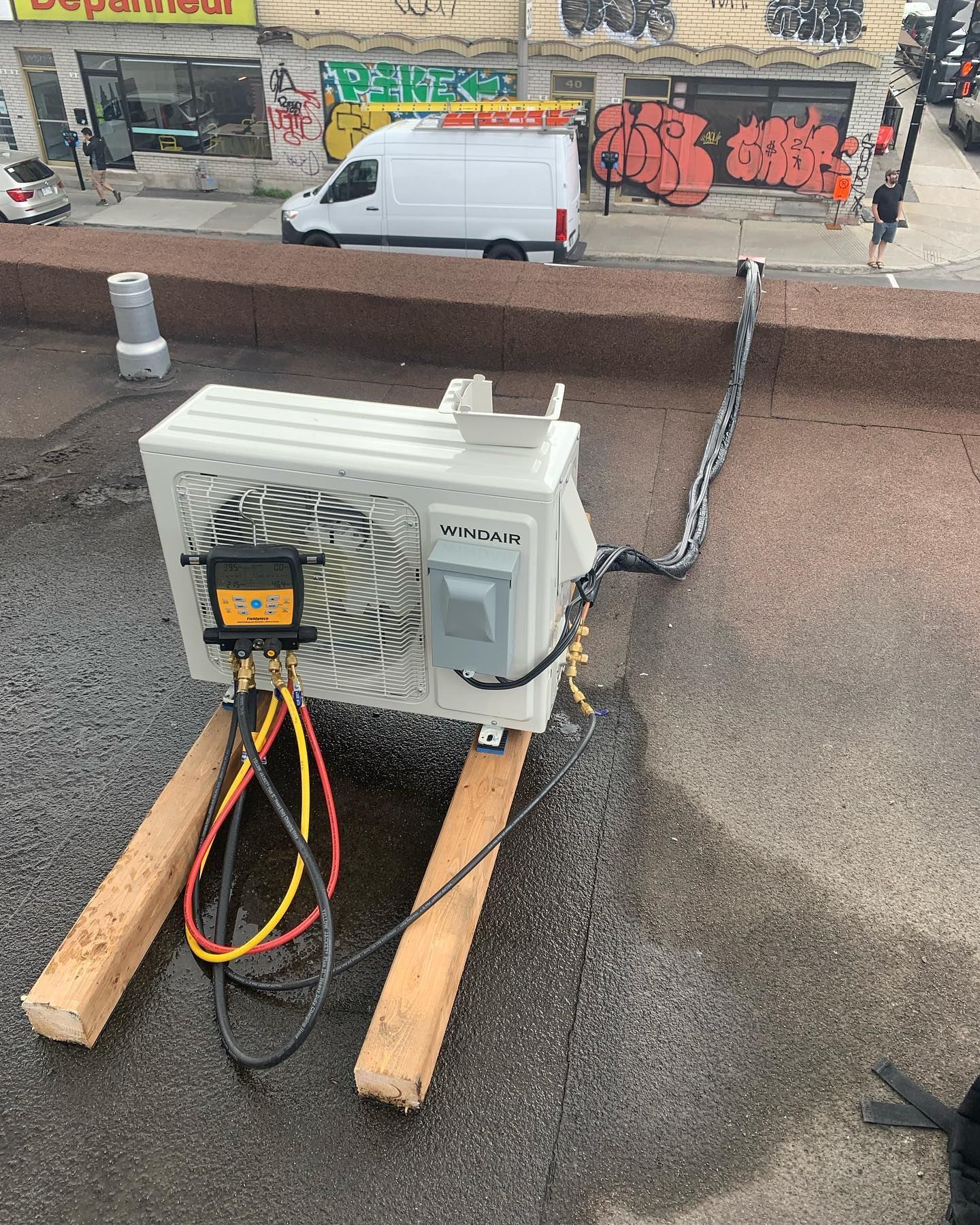 A white air conditioner is sitting on top of a wooden pallet on a roof.