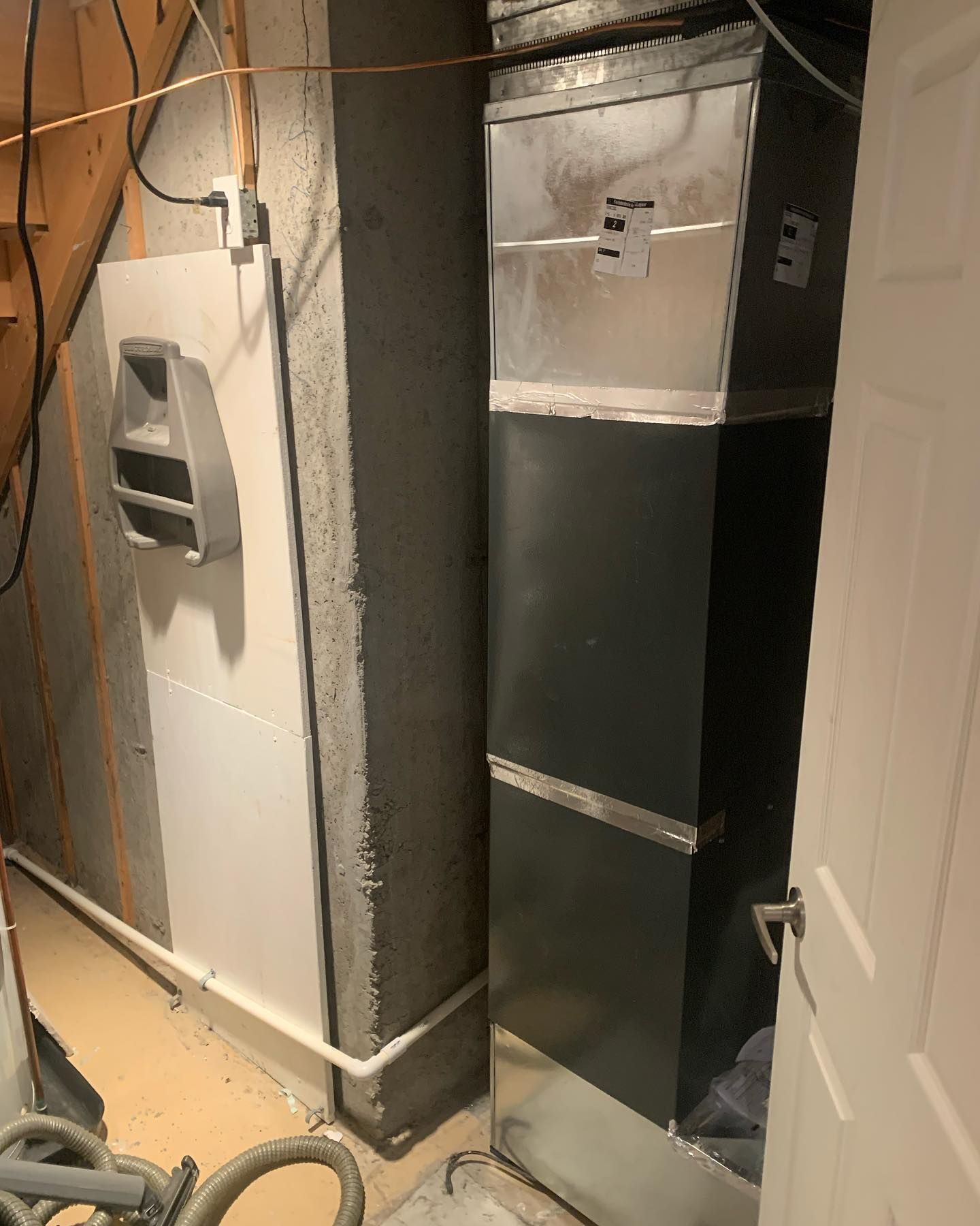 An air conditioner is sitting in a basement next to a staircase.