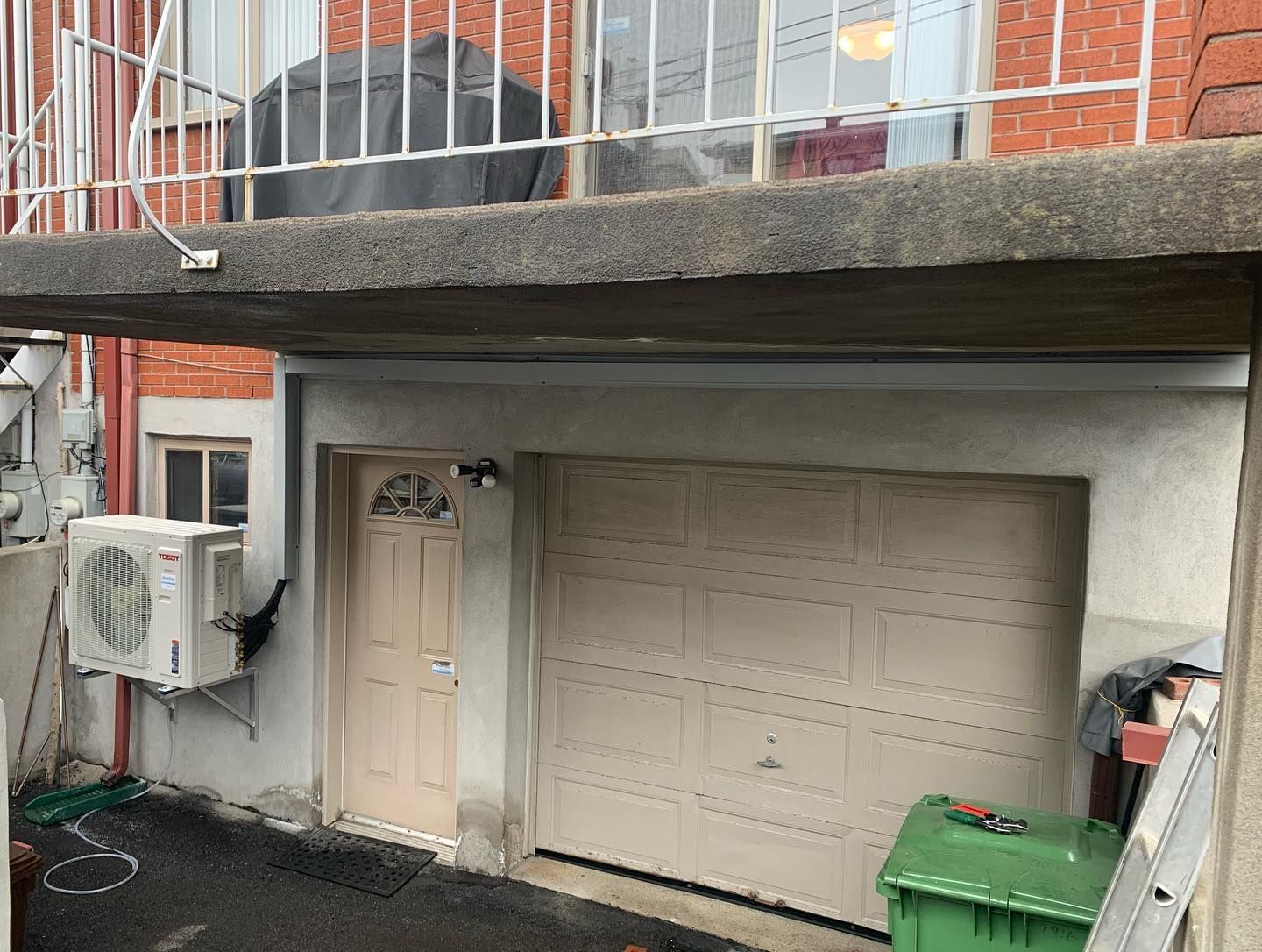 A garage door with a green trash can in front of it.