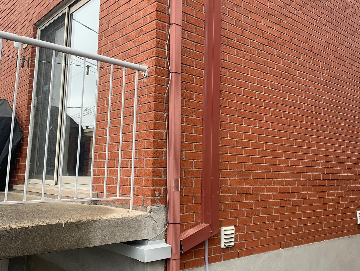 A brick building with a balcony and a drainpipe on the side.