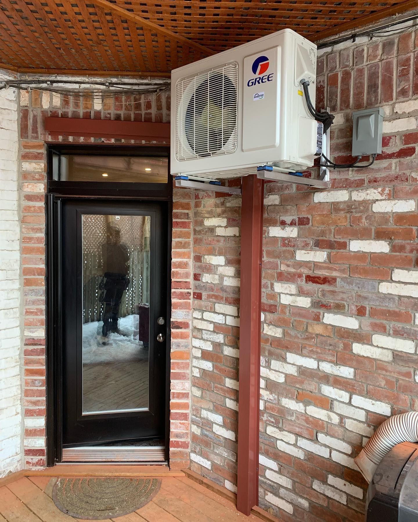 A large air conditioner is mounted on the side of a brick building next to a door.