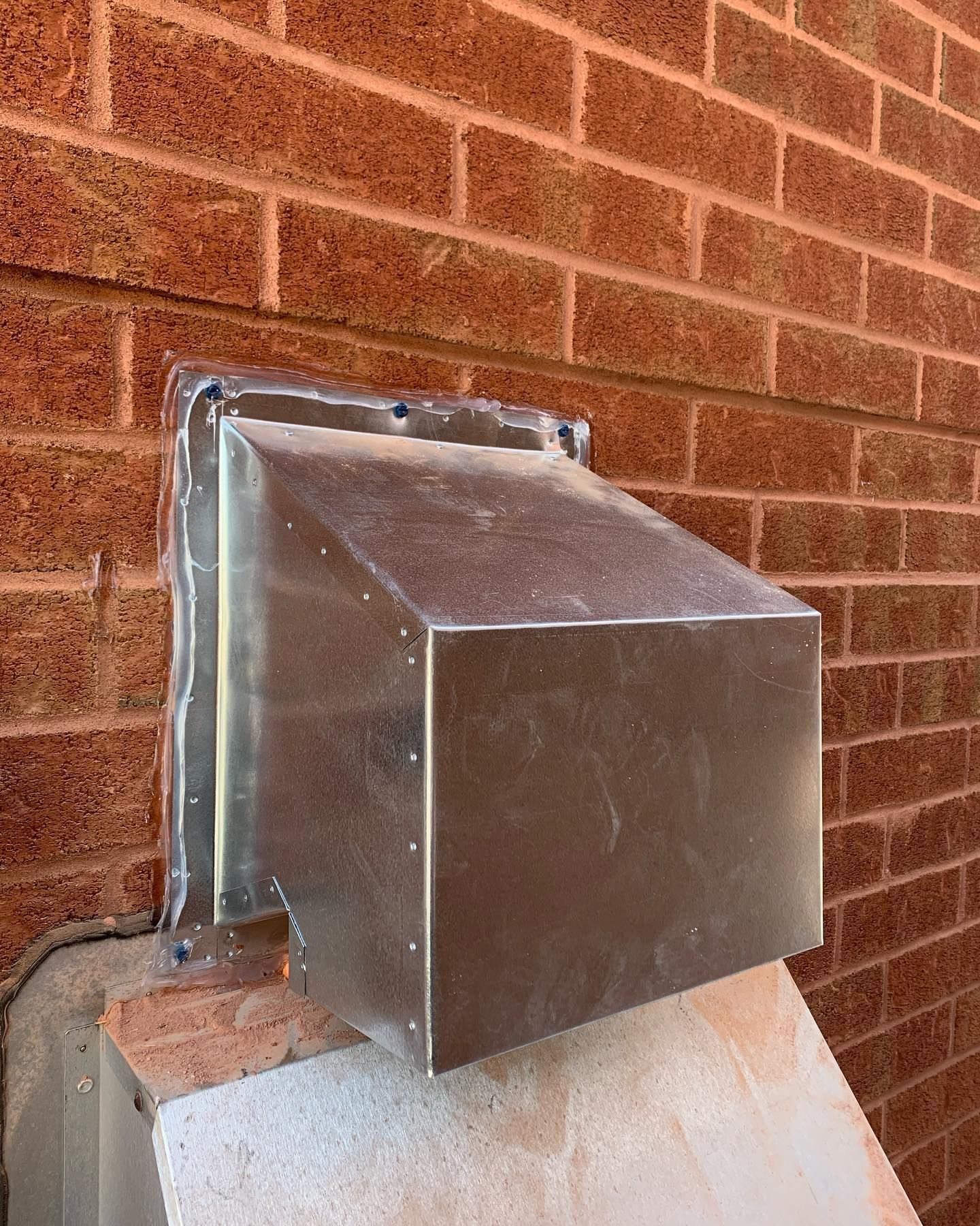 A metal box is attached to a brick wall.