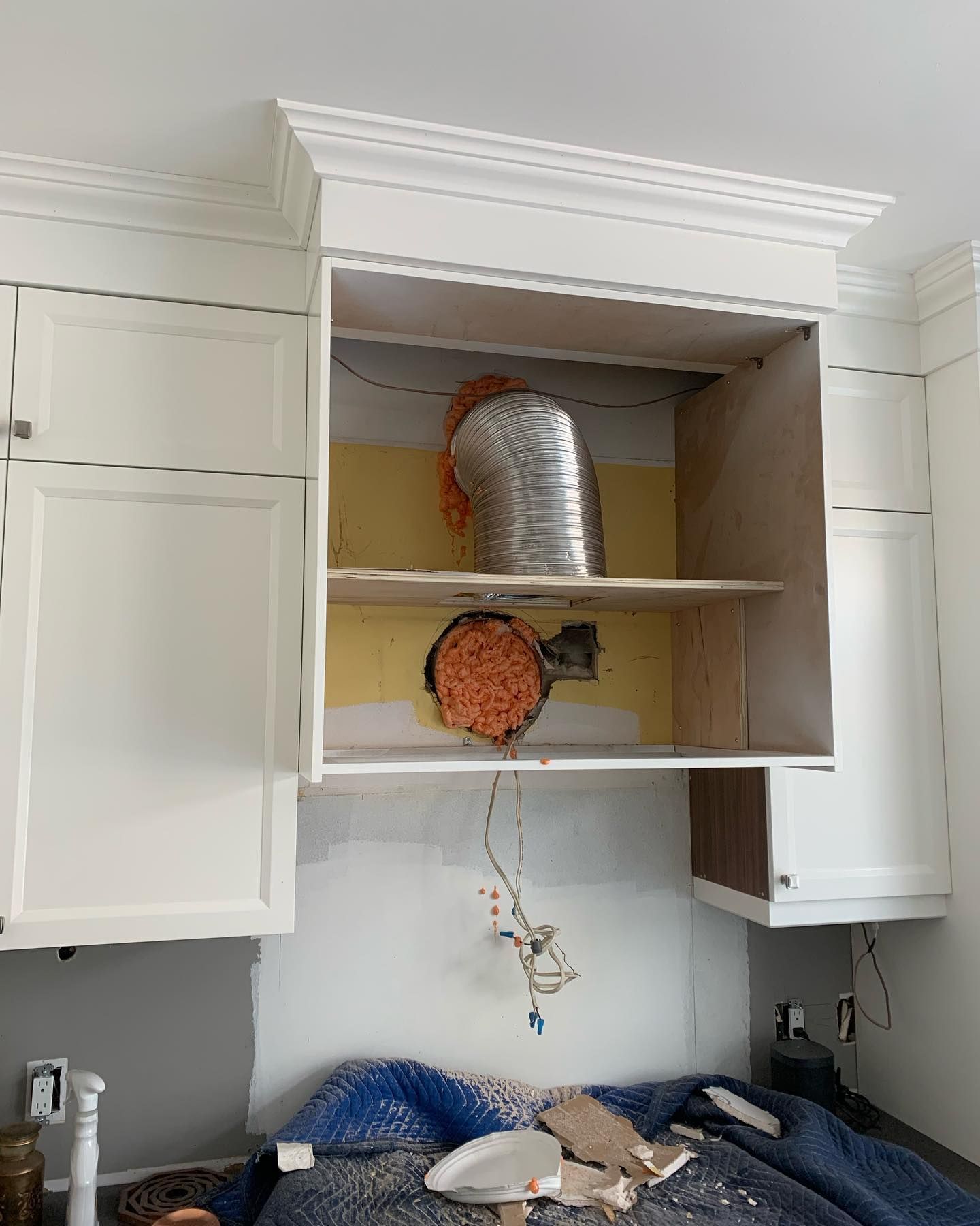 A kitchen with white cabinets and a hood being installed.