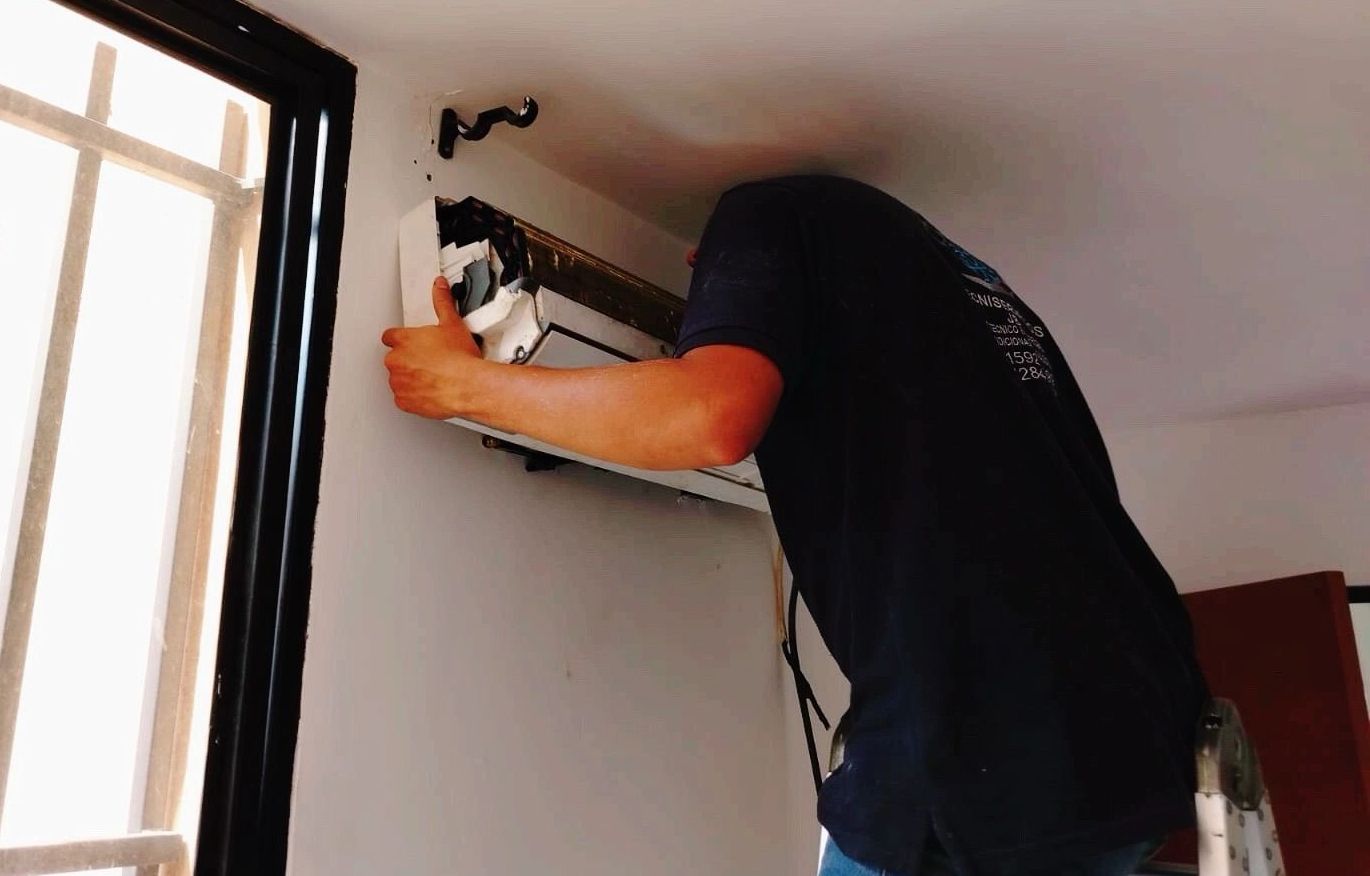 Un hombre con una camisa azul está trabajando en un aire acondicionado.