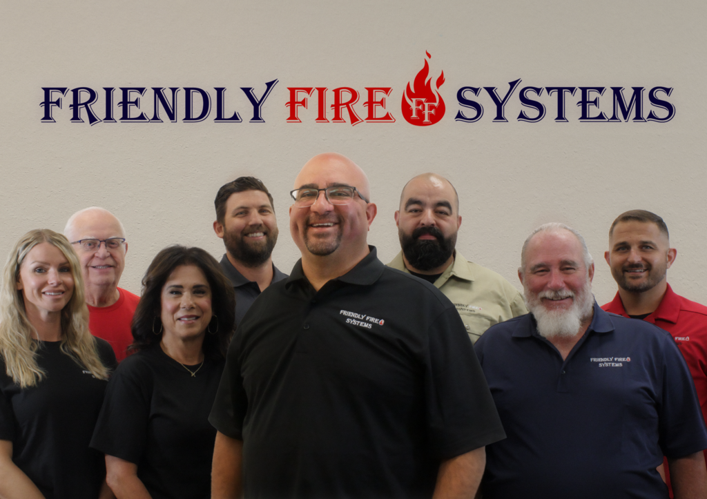 A group of people are posing for a picture in front of a wall that says friendly fire systems.