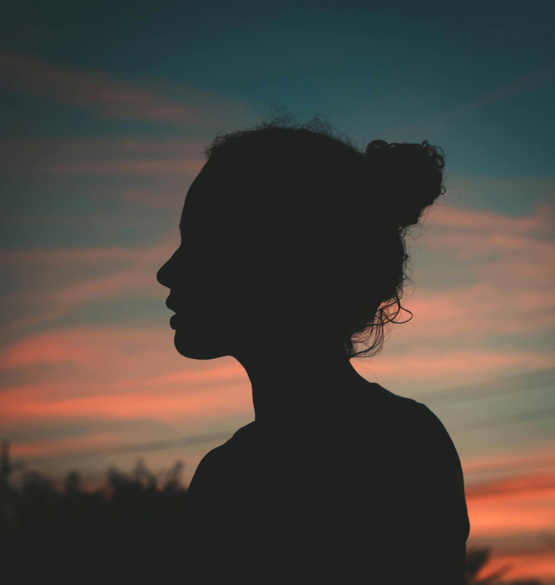 Silhouette of person with bun hairstyle, gazing left, against a colorful sunset backdrop.