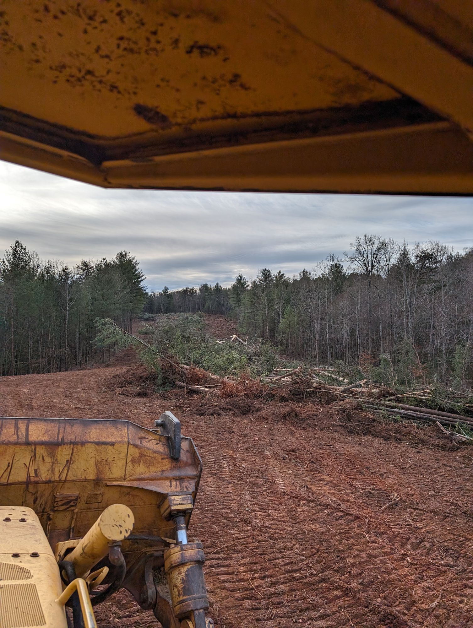 Bulldozer cab view over a muddy cleared forest road under an overcast sky