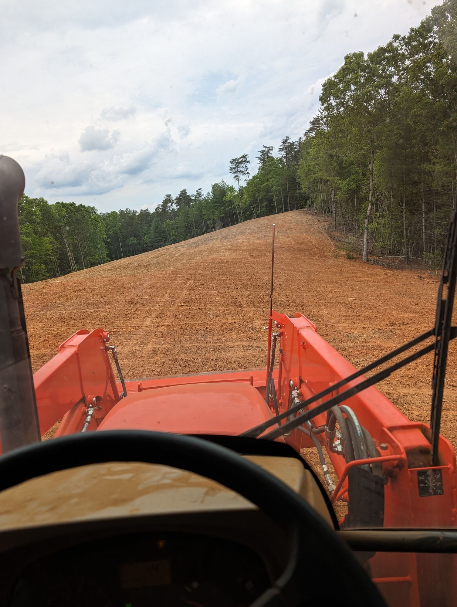 View from a tractor driving on a dirt road through a wooded area under cloudy skies
