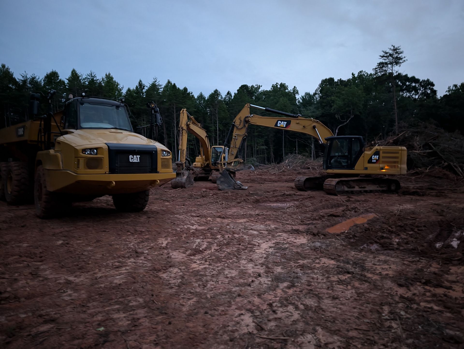 Three yellow excavators on a muddy construction site at dusk
