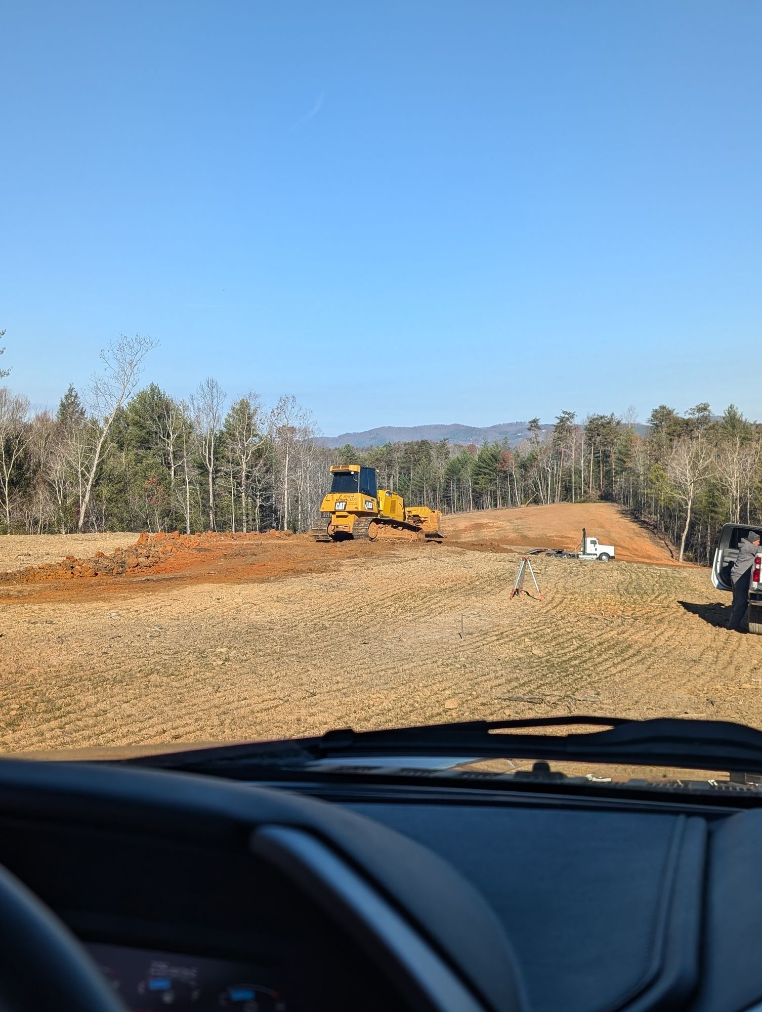 Yellow bulldozer grading dirt on a roadside construction site, viewed from inside a car