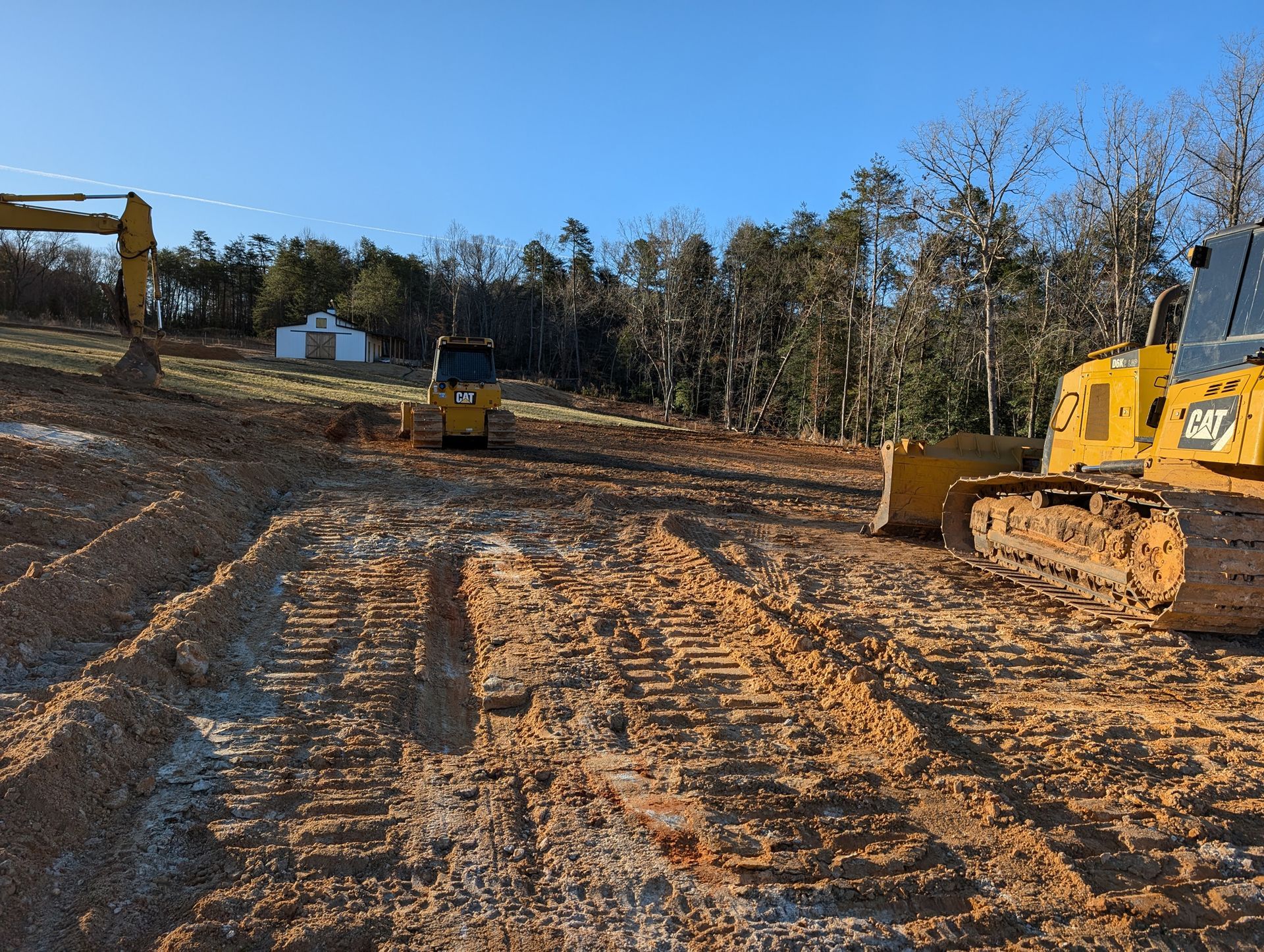 Construction site with yellow bulldozer on muddy dirt road and trees in the background