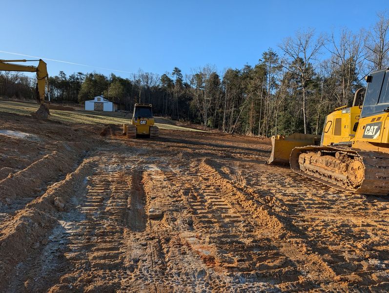 Construction site with yellow bulldozer on muddy dirt road and trees in the background