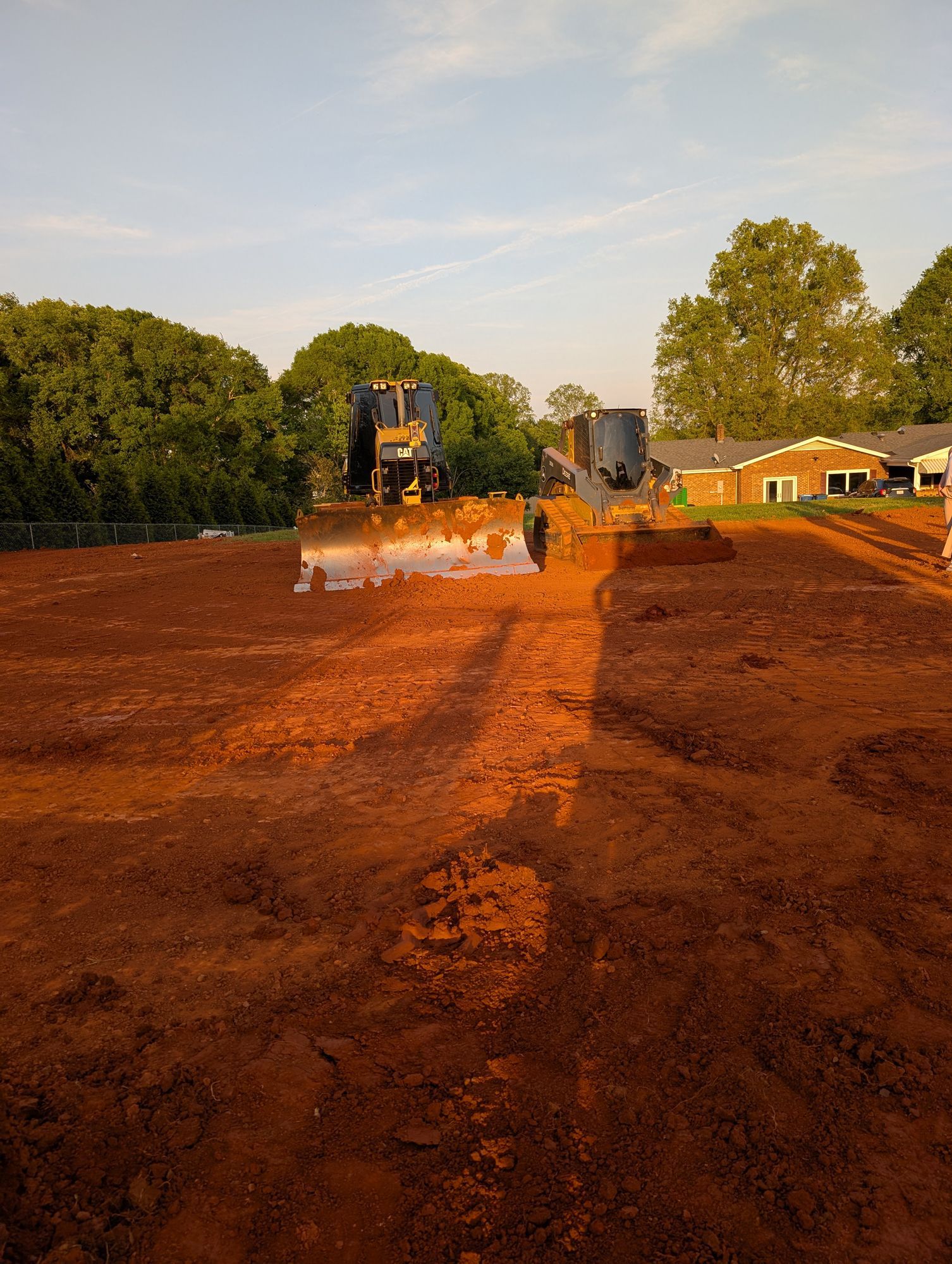 Bulldozer leveling red dirt on a construction site at sunset