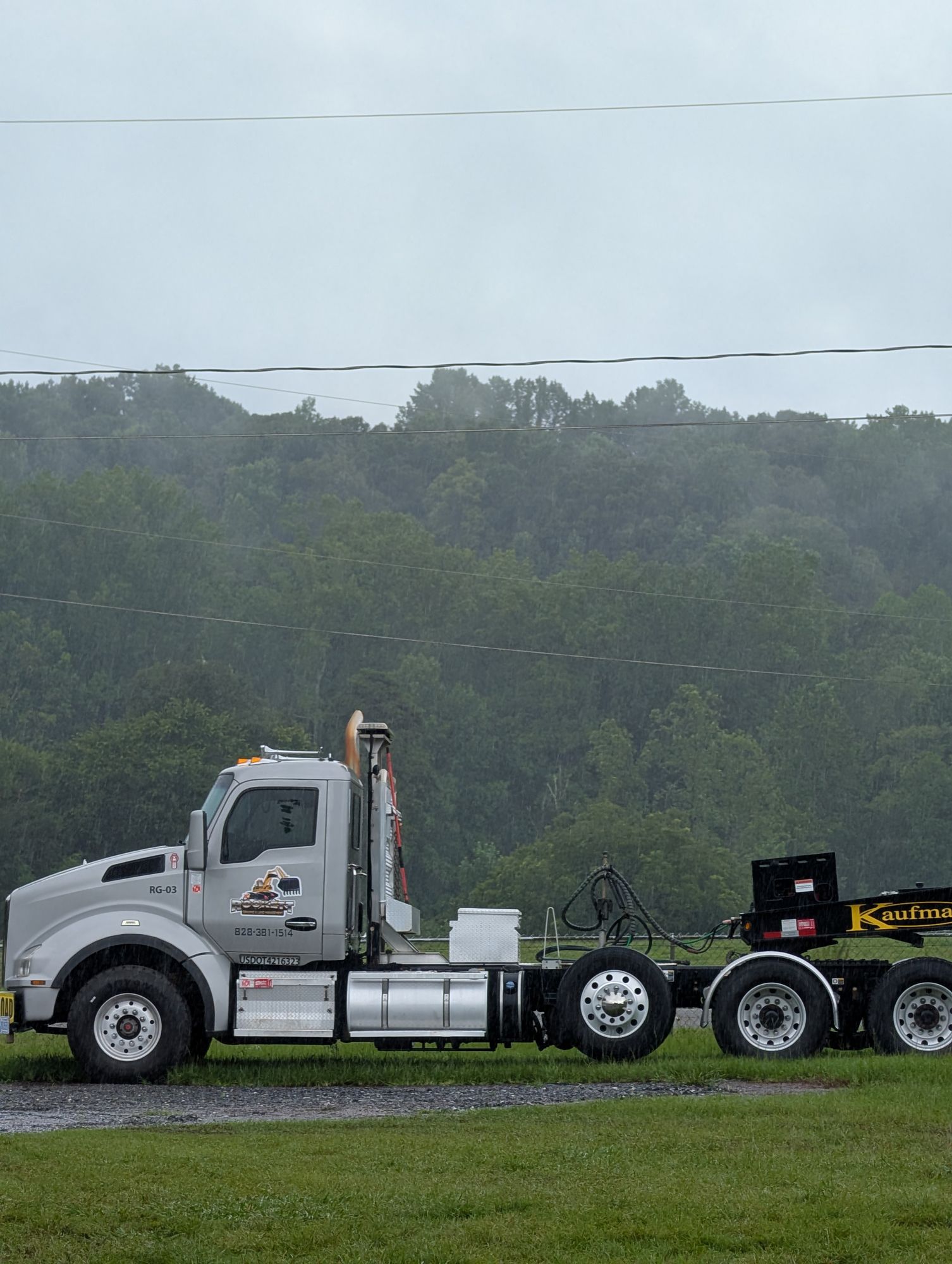 White semi-truck cab and chassis parked on a wet road near grassy fields under a cloudy sky.