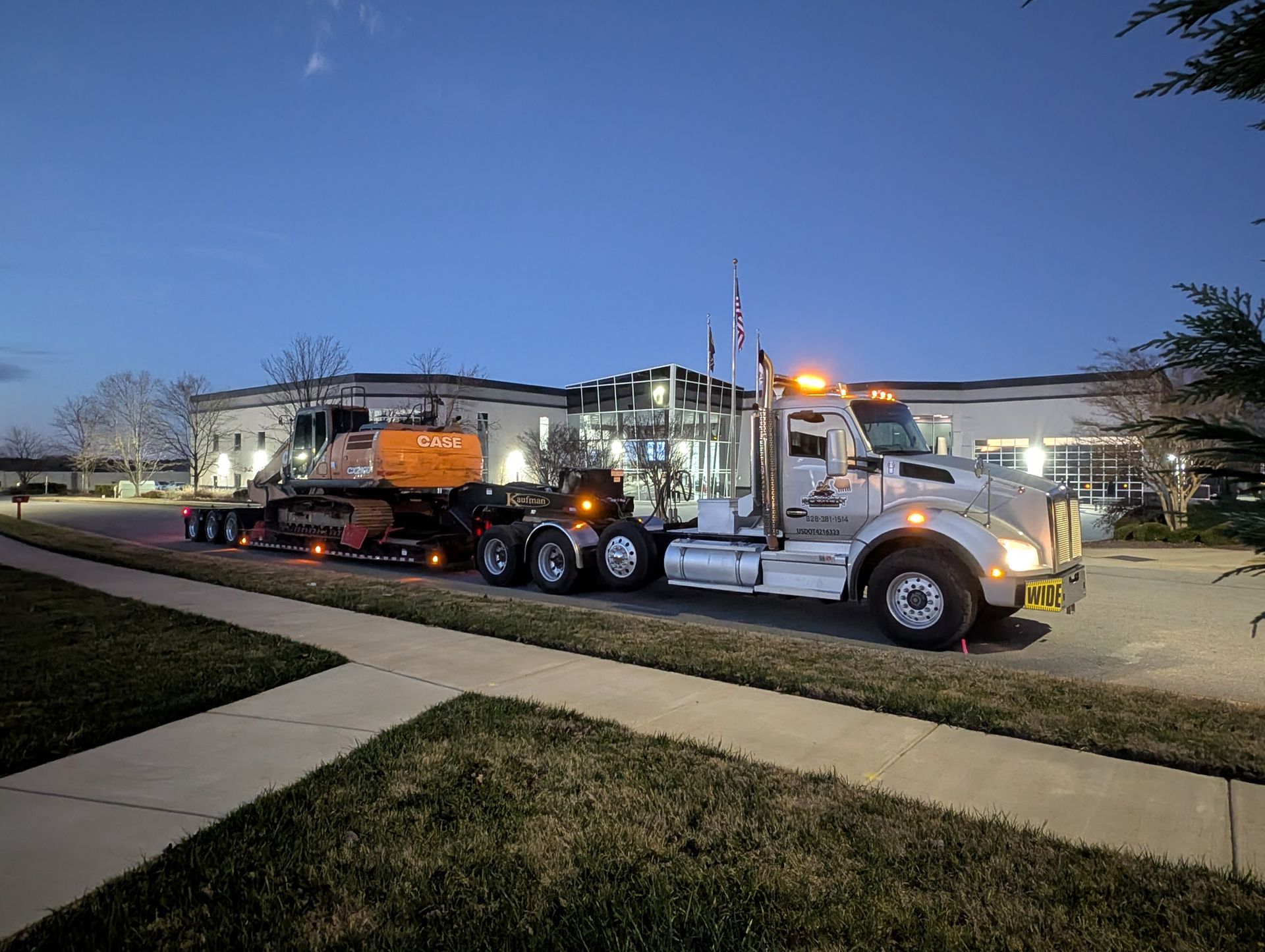 Two semitrucks parked outside a building at dusk, one with amber lights on