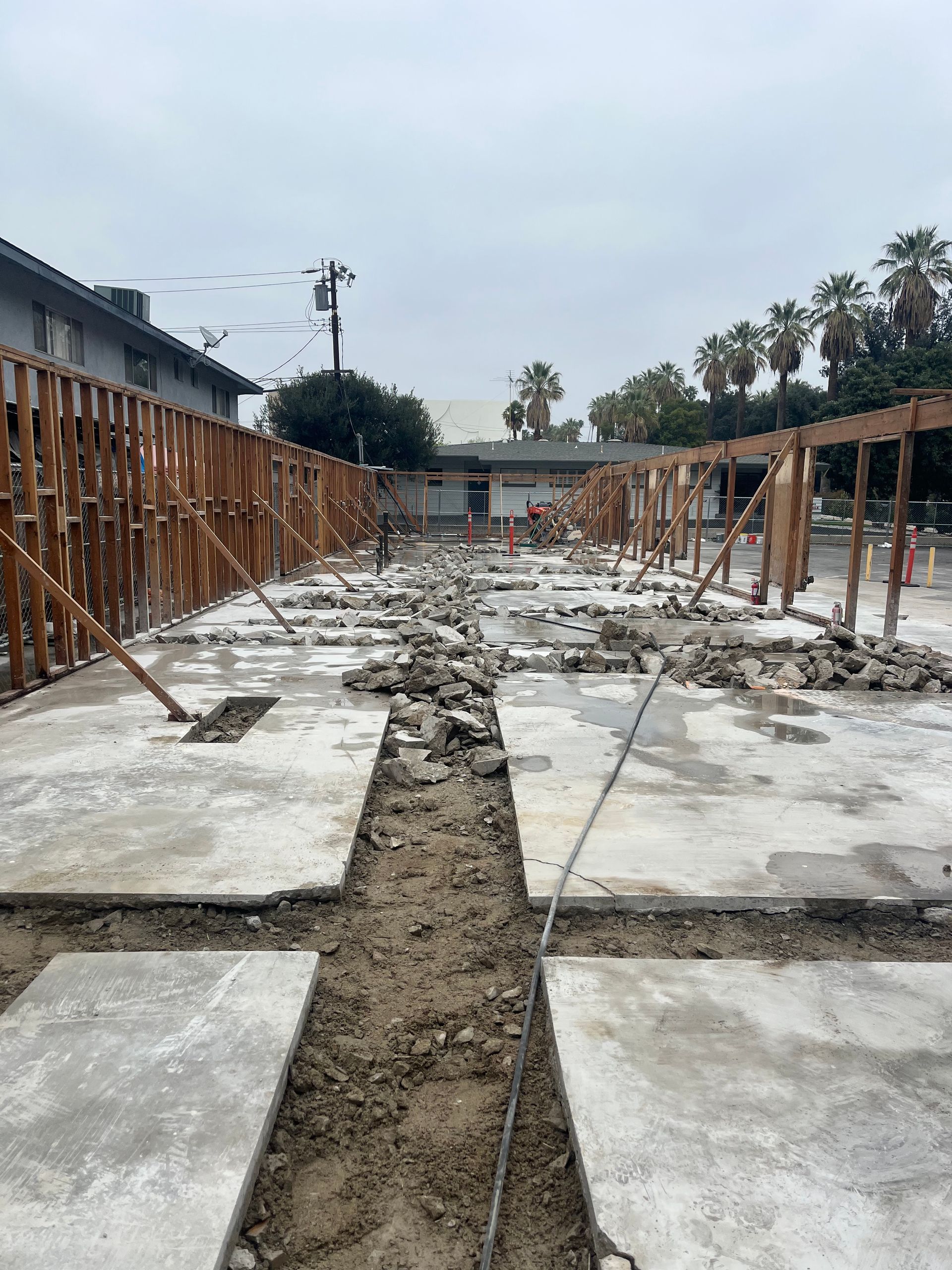 Construction site showing a long, narrow strip of exposed earth between two sections of concrete slabs and wood framing.