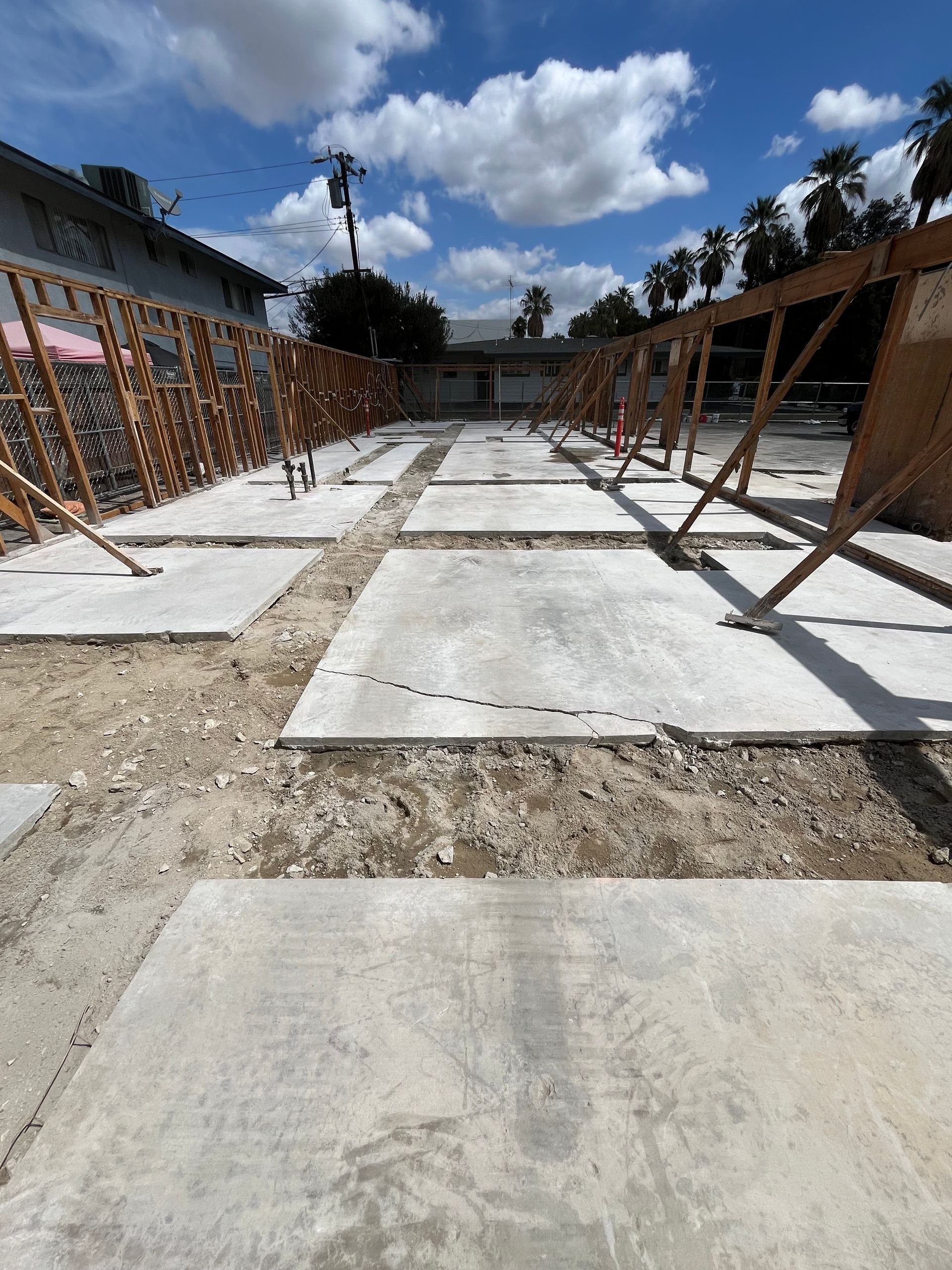 Construction site with multiple concrete pads, wooden wall framing, and scaffolding under a blue, cloudy sky.