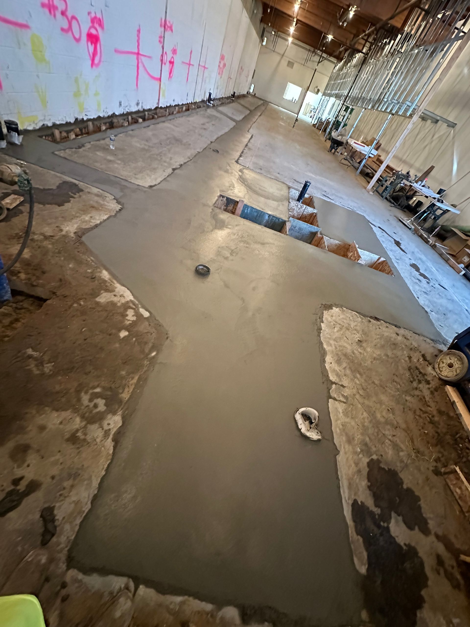 A construction site with wet, freshly poured concrete filling trenches in an existing concrete floor.
