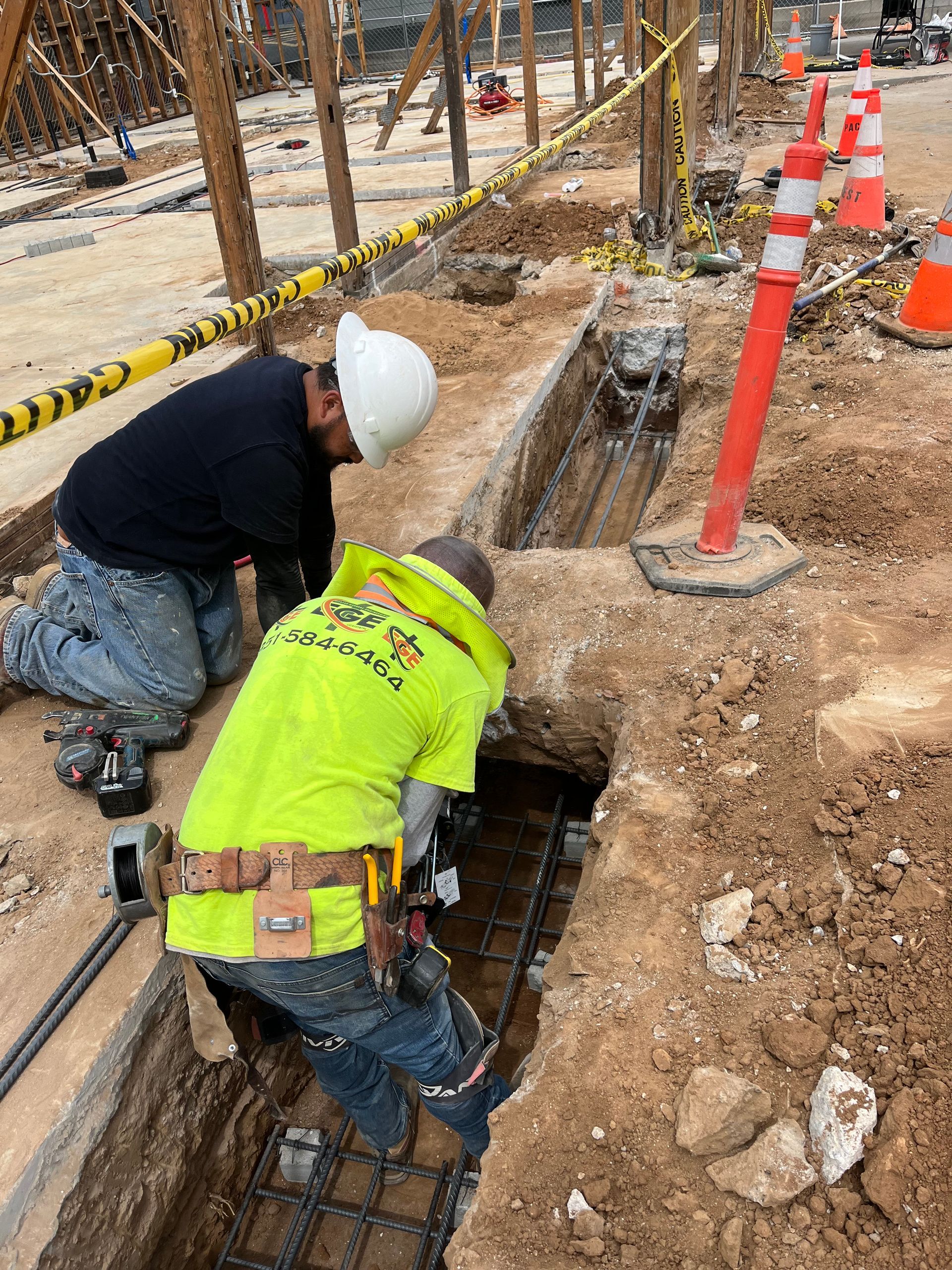 Two workers in hard hats and high-visibility gear installing rebar in a construction trench.