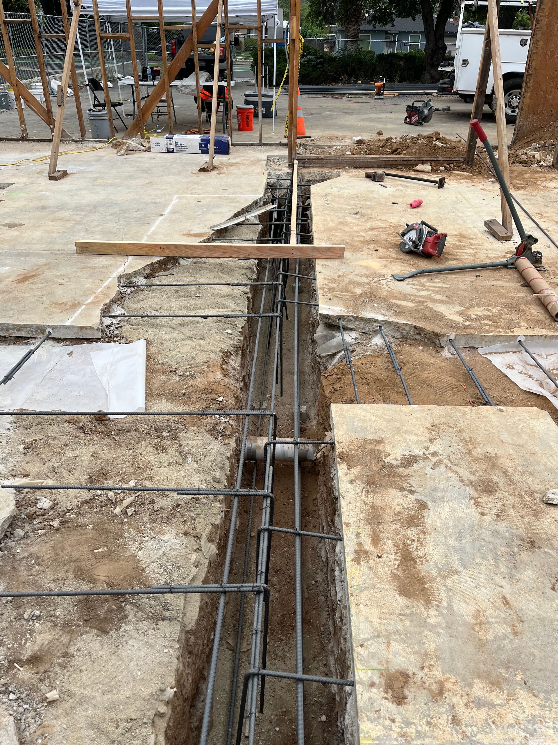 A narrow trench in a concrete floor contains rebar framework for a foundation beam at a construction site.