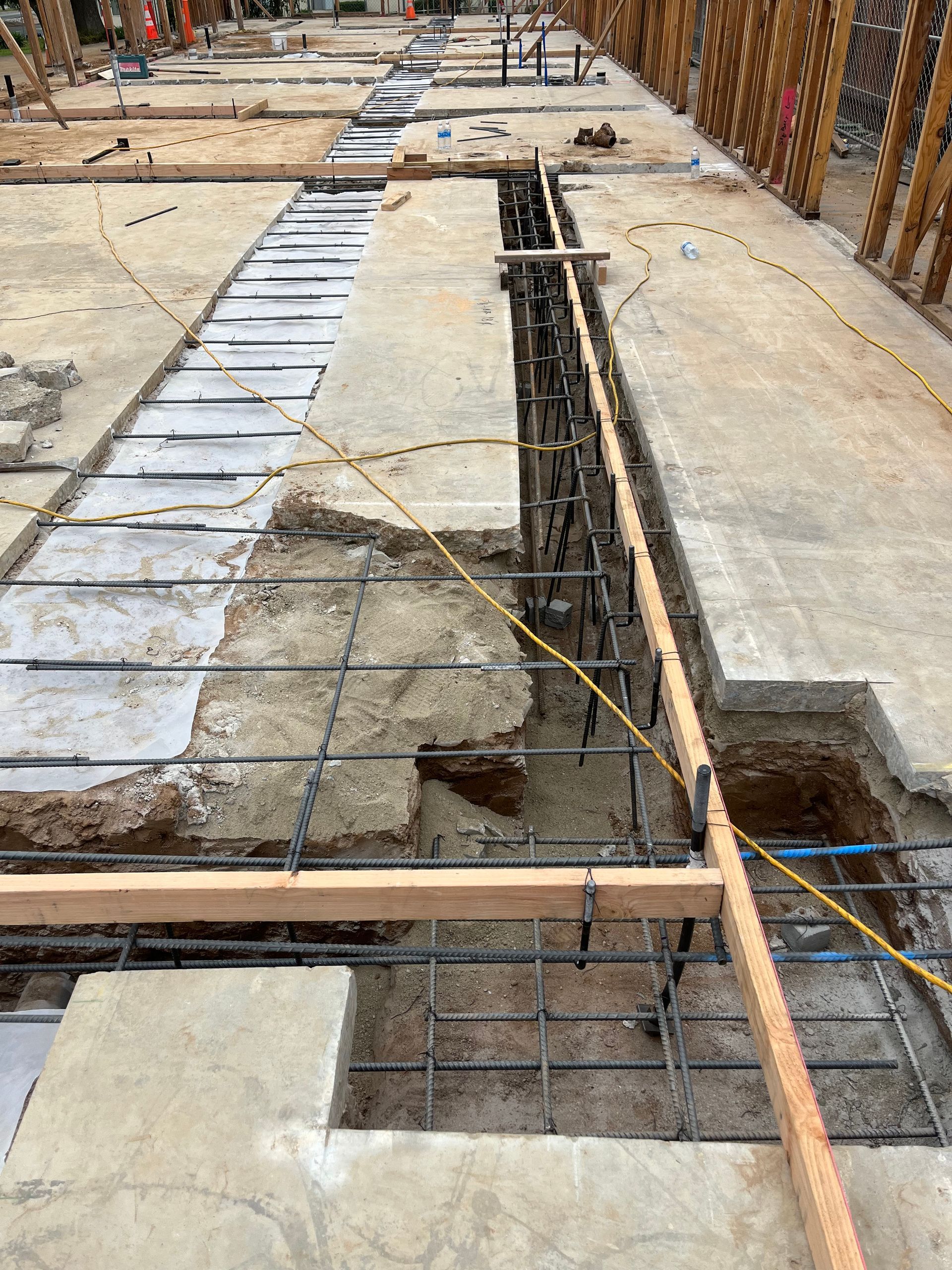 A construction site showing concrete slab preparation with exposed steel rebar framework in trenches for a foundation.