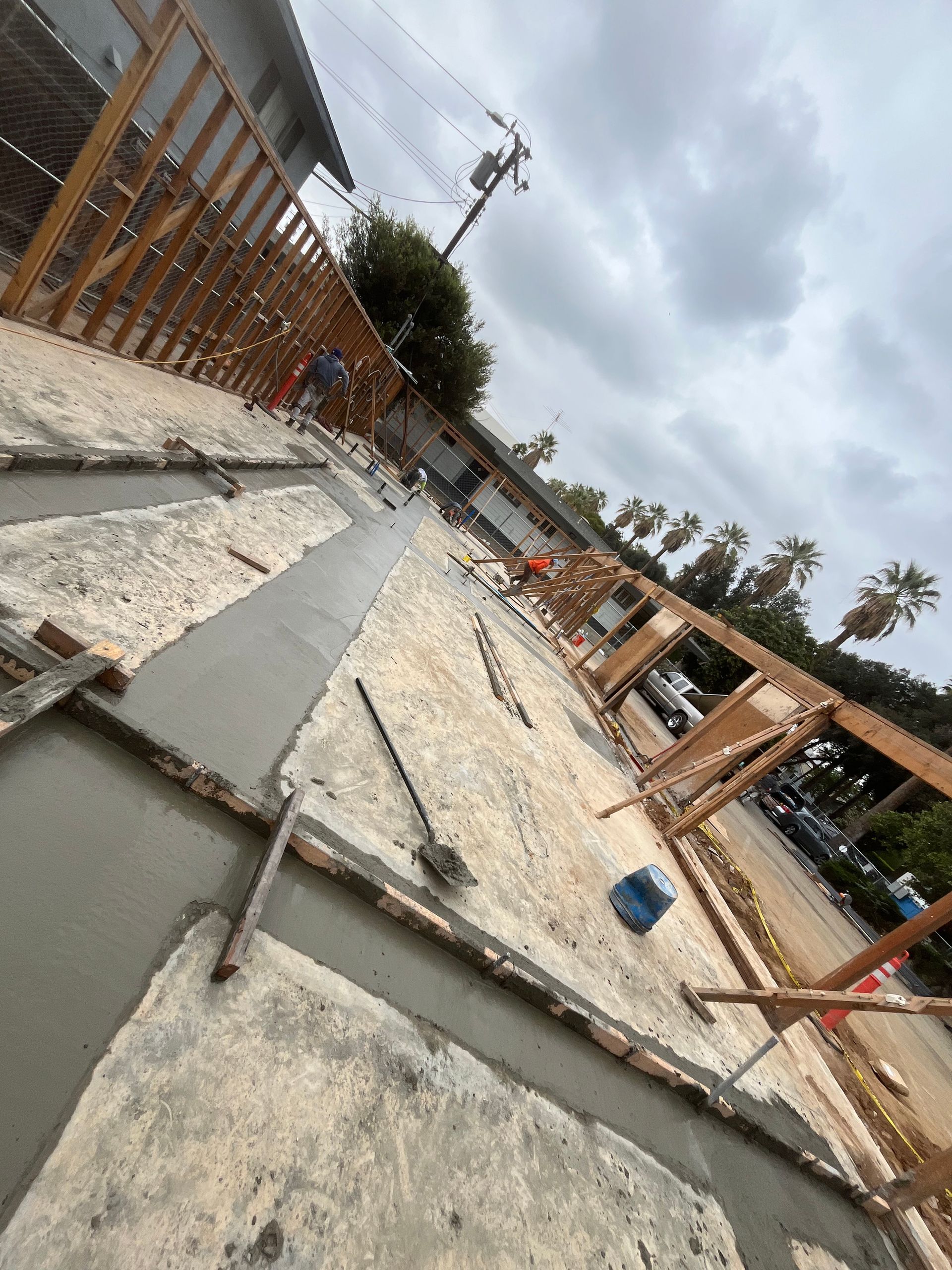 An outdoor construction site featuring wooden framing on a concrete foundation with freshly poured mortar strips.
