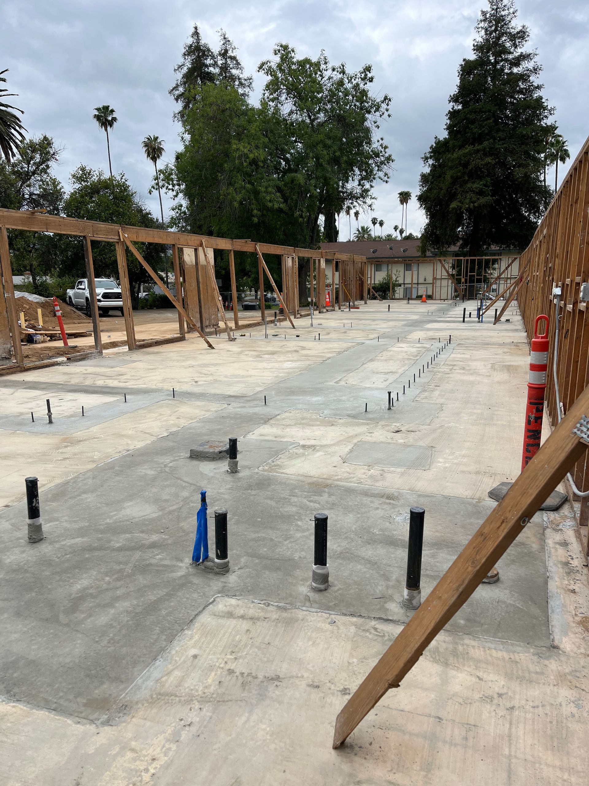Concrete slab foundation for a building under construction, featuring exposed plumbing pipes and wooden framing walls.