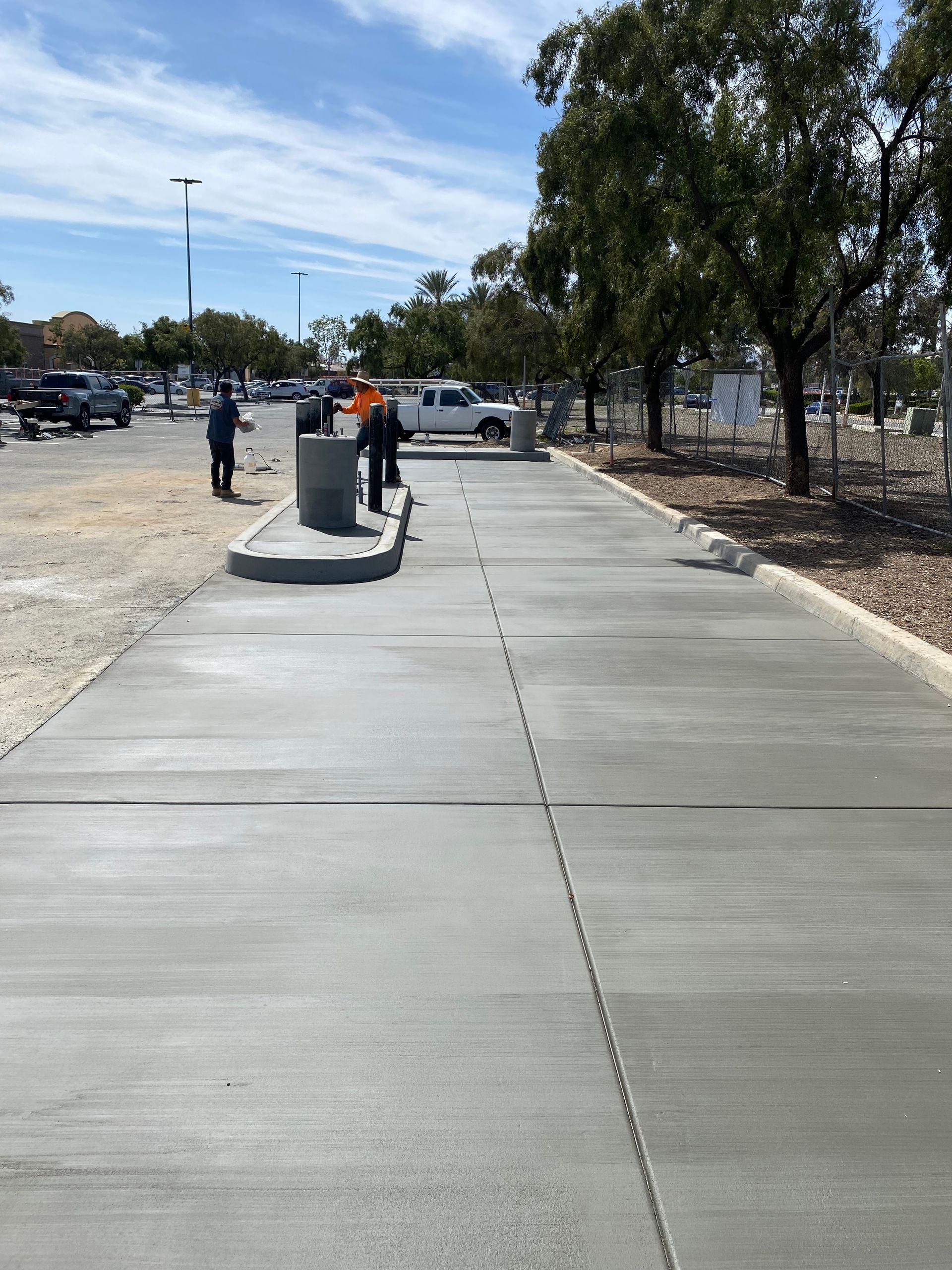 A freshly poured concrete sidewalk in an outdoor parking area with workers nearby.