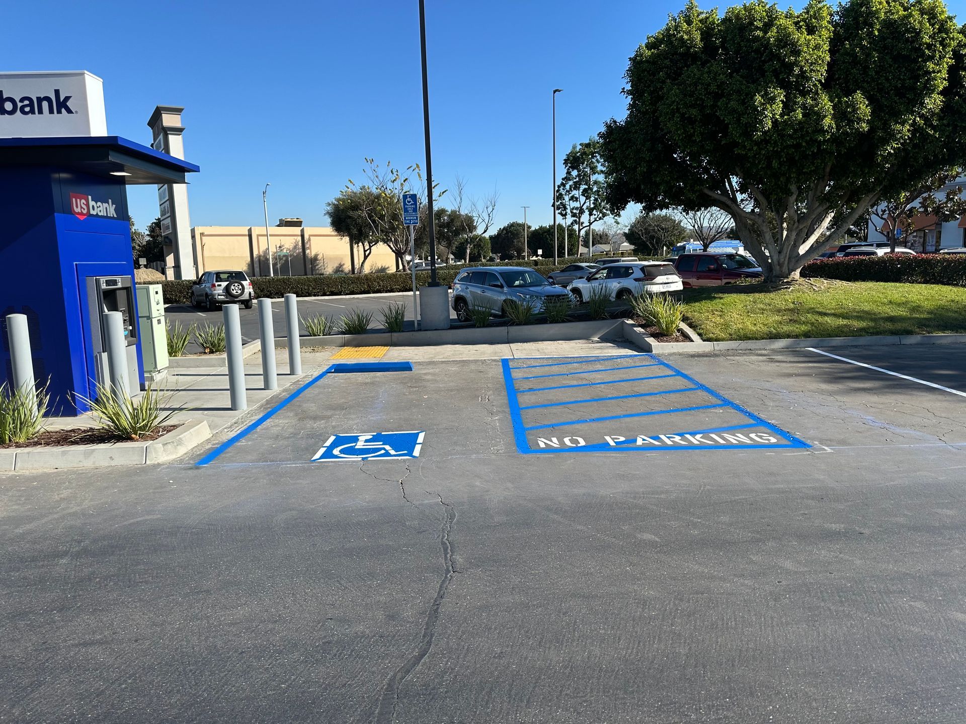 A blue-painted handicap parking space with an adjacent marked no-parking loading zone next to a bank ATM.