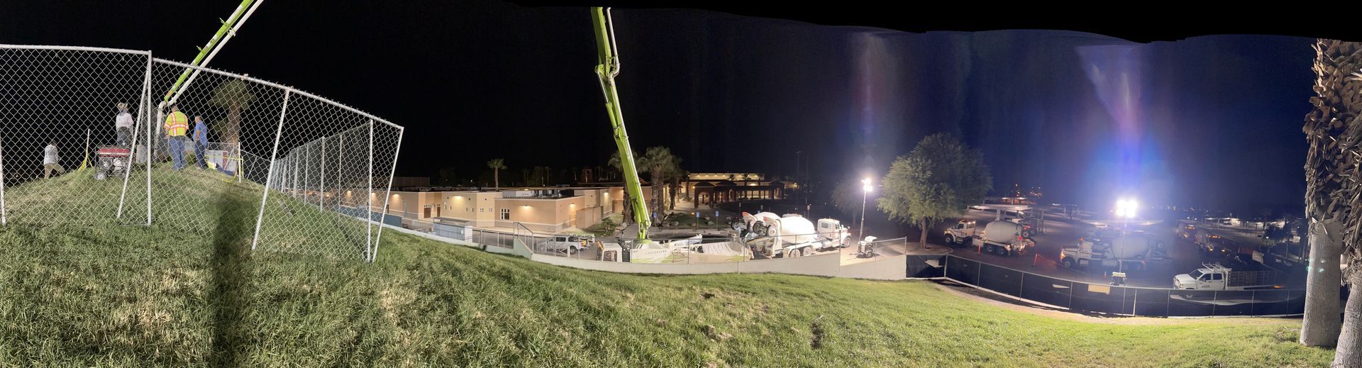 A night construction site featuring a tall crane and concrete mixer truck illuminated by bright stadium-style work lights.