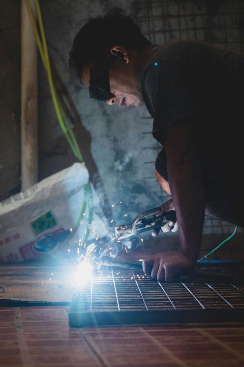 A man is welding a piece of metal in a dark room.