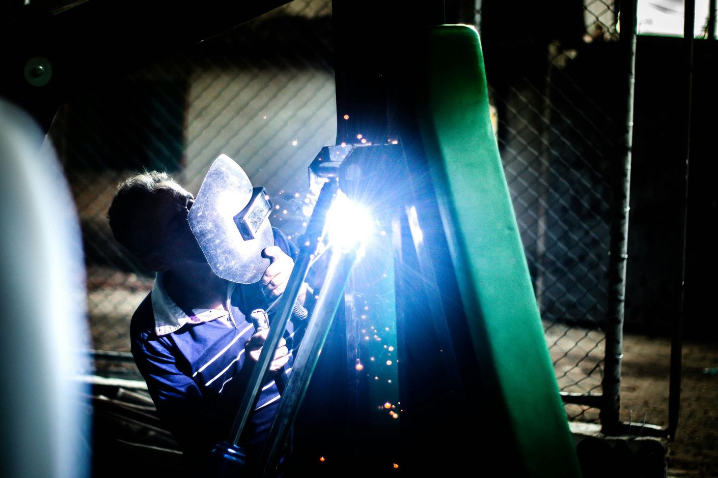 A man is welding a green object in a dark room