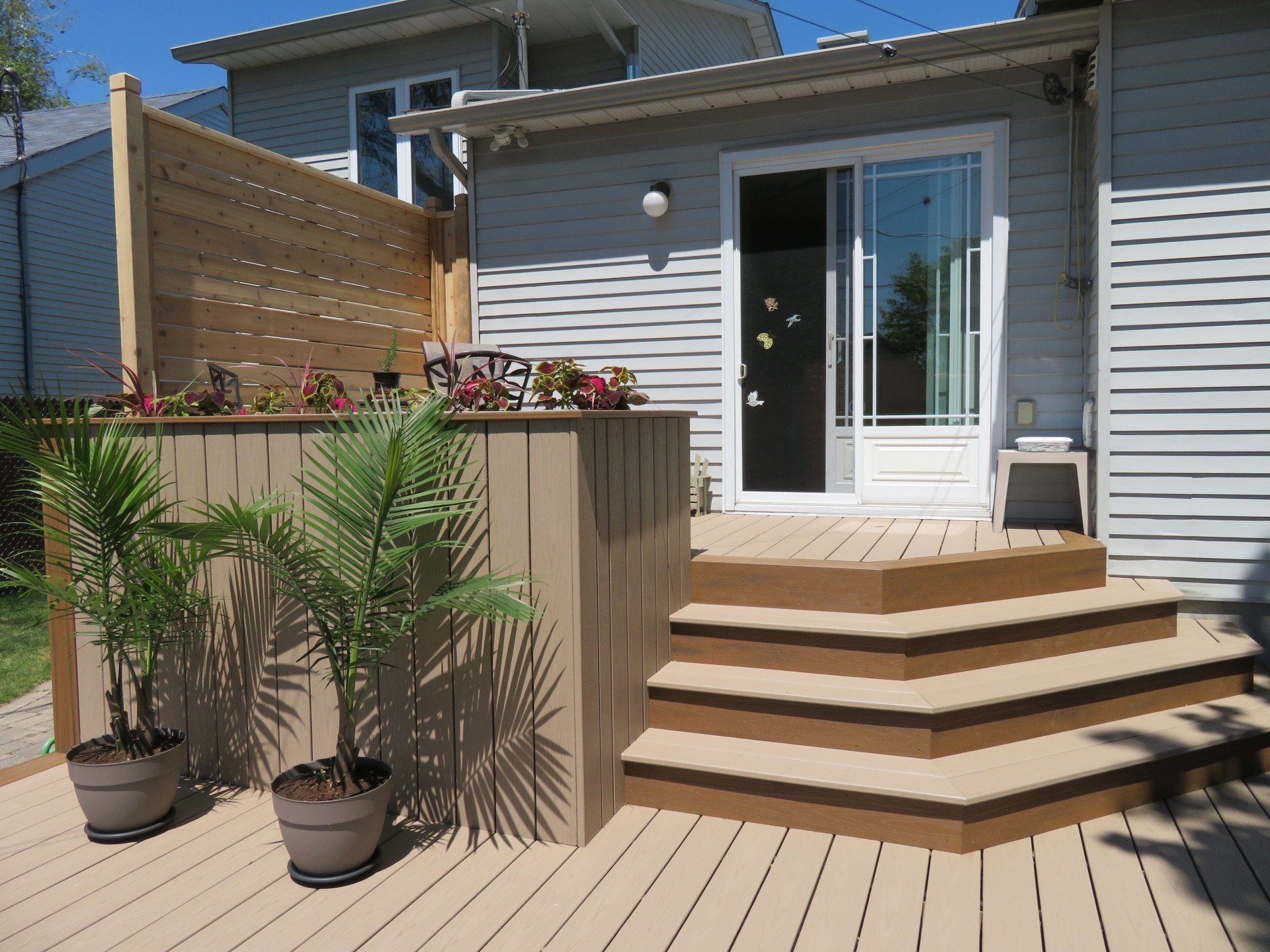 Une terrasse en bois avec des escaliers et des plantes en pot devant une maison.