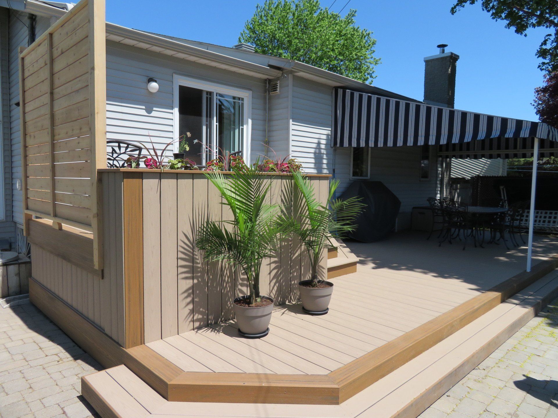 Une terrasse en bois avec des plantes en pot devant une maison