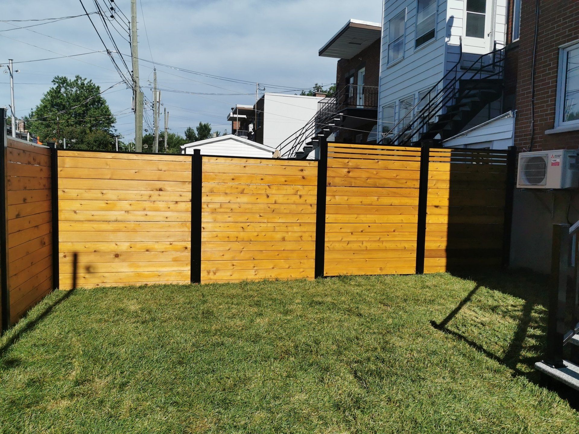 A wooden fence surrounds a lush green yard in front of a house.