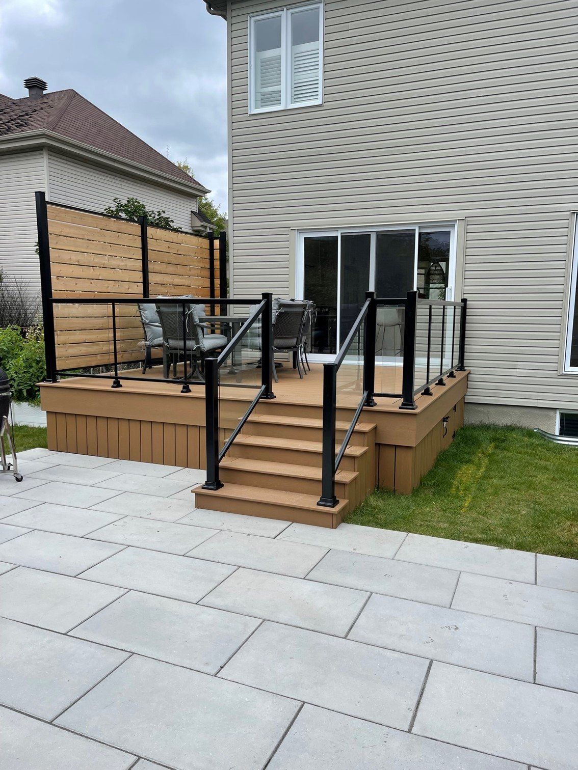 A wooden deck with stairs and a glass railing in front of a house.