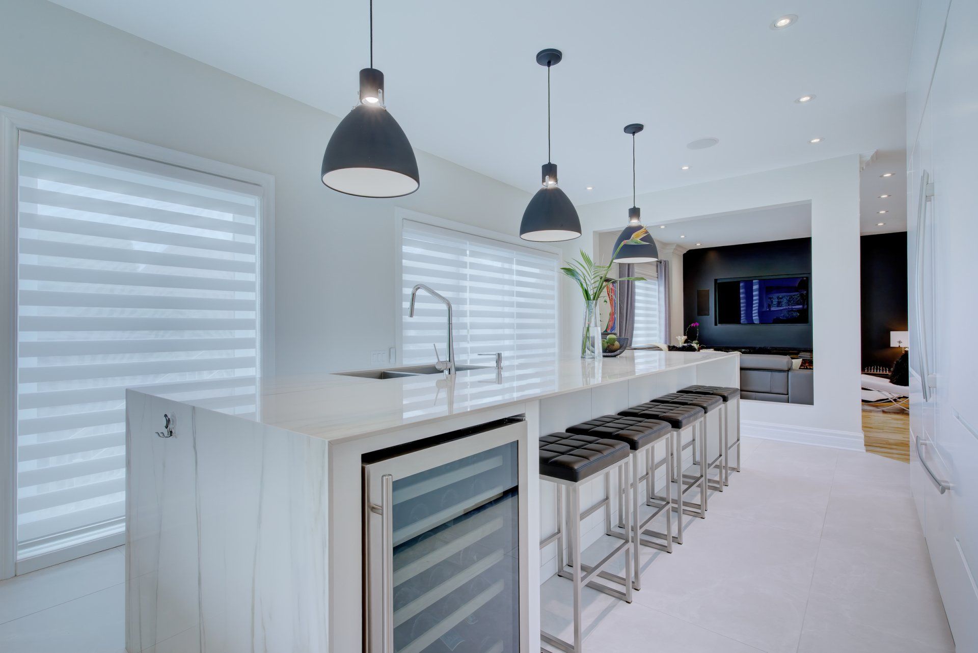 A kitchen with a long island , stools and a wine cooler.