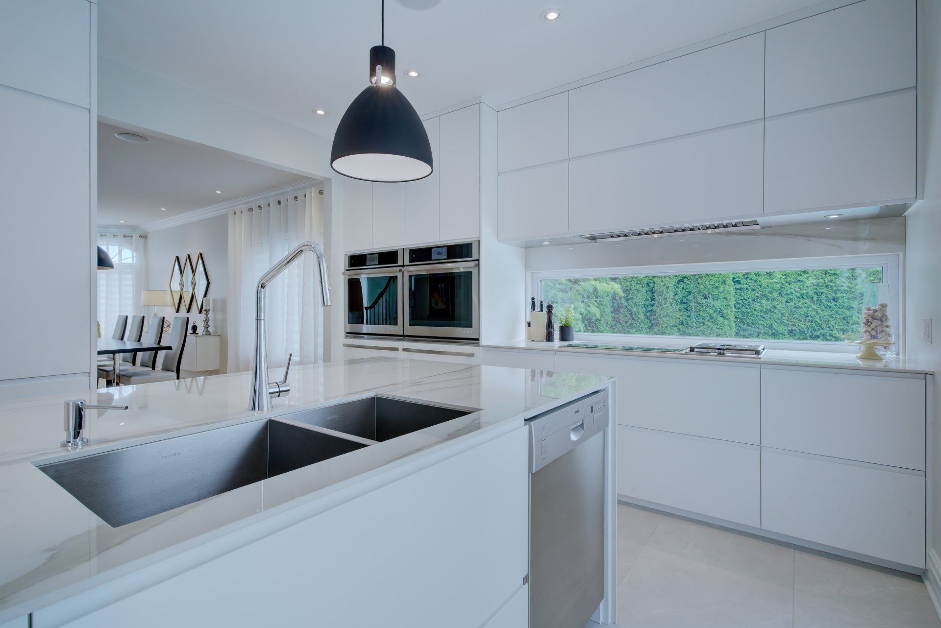 A kitchen with white cabinets , stainless steel appliances , a sink and a window.