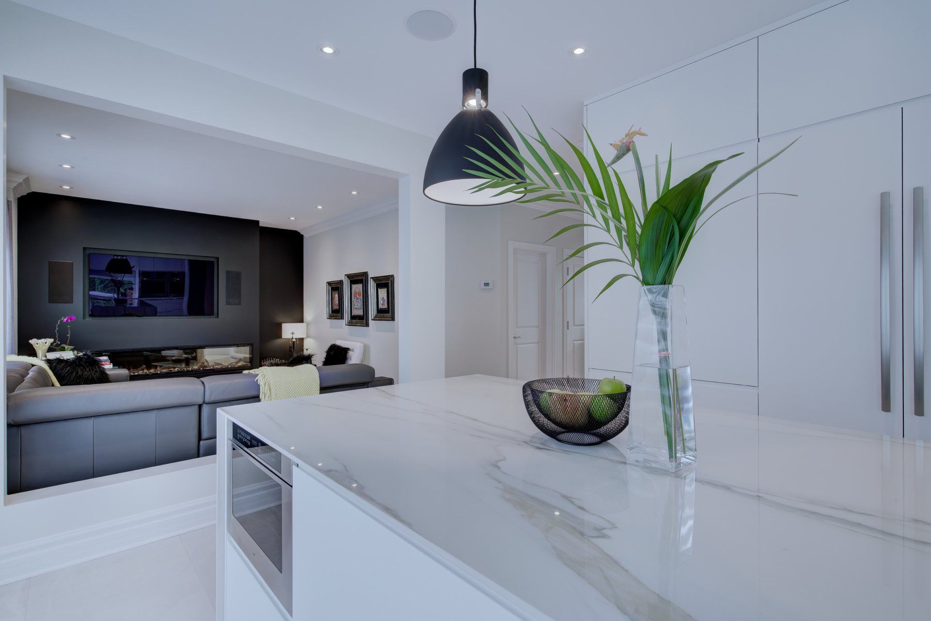 A kitchen with a vase of flowers on the counter and a living room in the background.