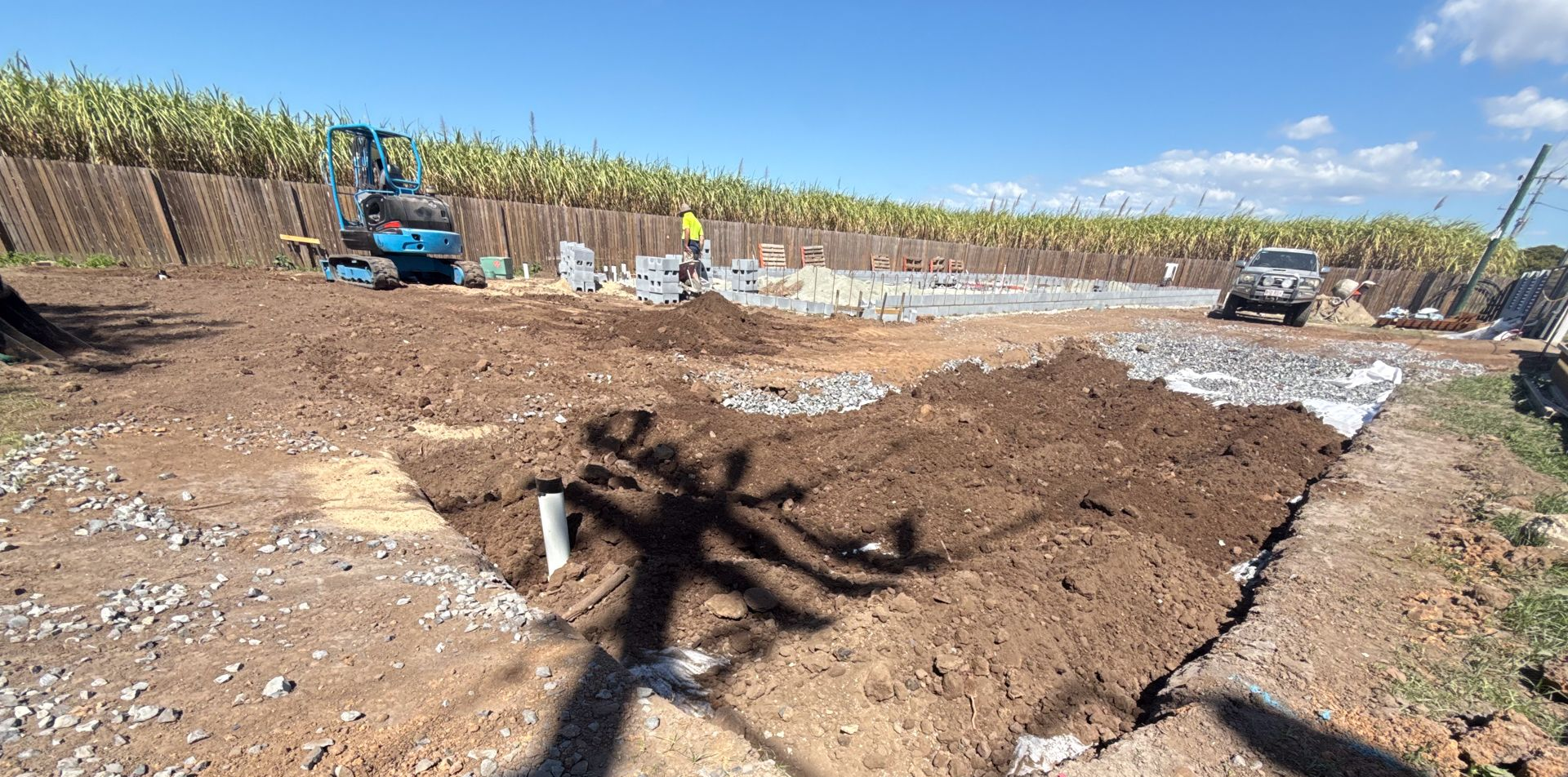 Construction site with heavy machinery, dirt piles, and a blue sky in the background.