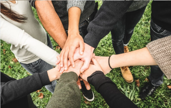 A group of people standing in a circle outdoors with their hands stacked together in the center.