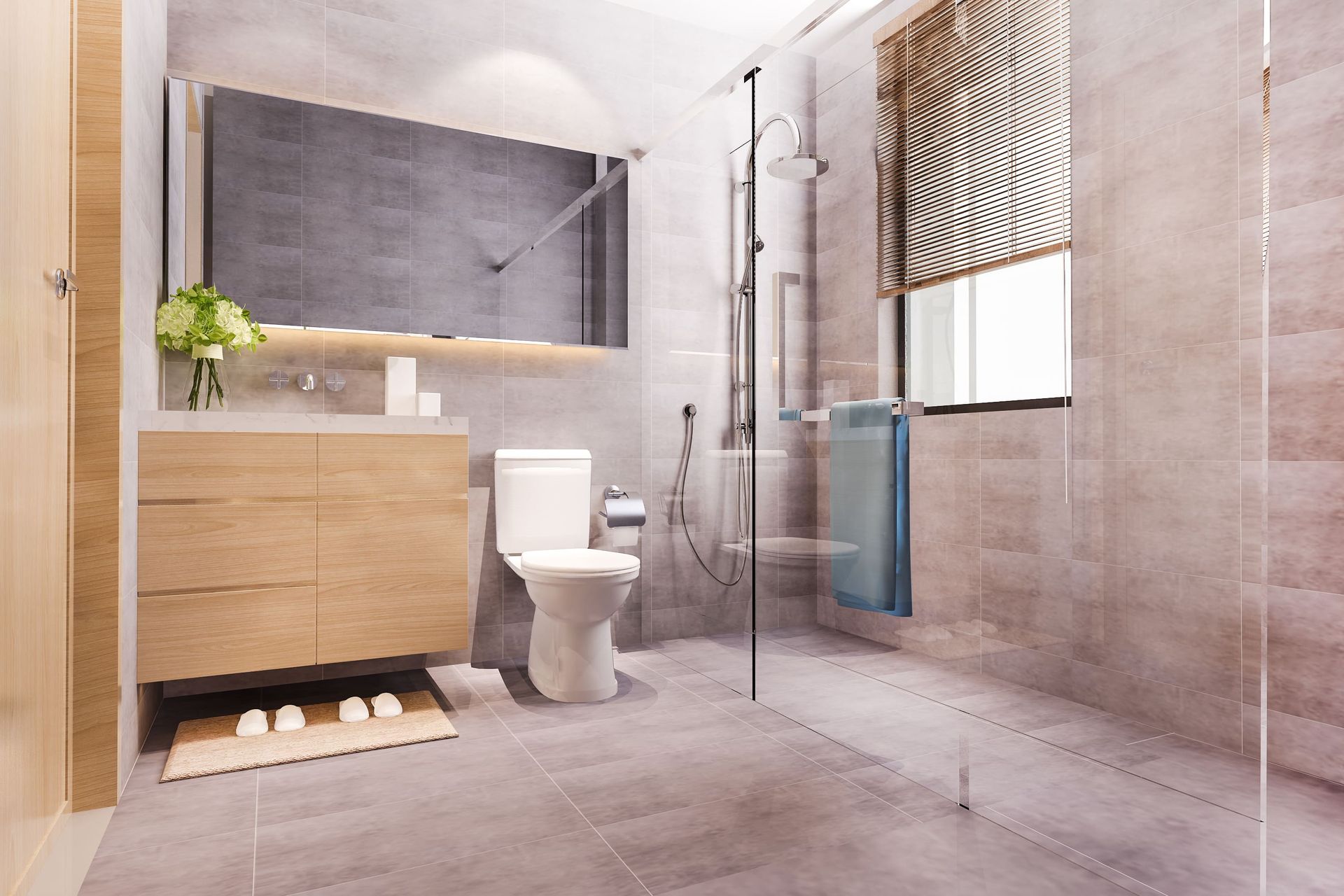 Modern bathroom with gray tile walls and floors. A white tub, toilet, and vanity sit in the space, with gold fixtures and a backlit mirror.