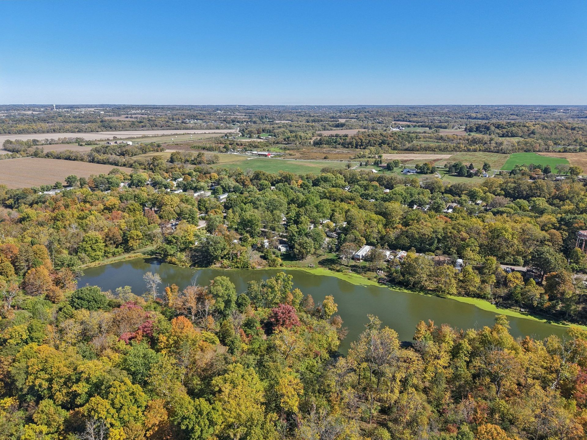 Aerial view of a lake surrounded by fall foliage and a small town under a blue sky.
